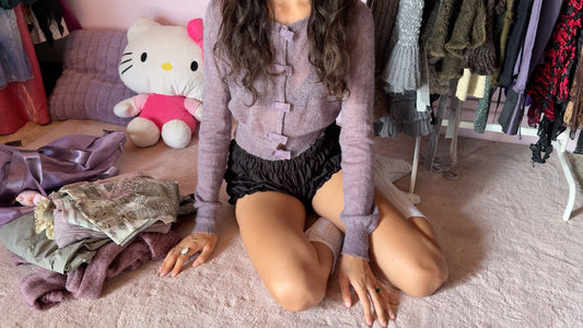 Woman sitting on carpet surrounded by vintage clothes — illustrating the chaos of thrift shopping. Discover curated vintage clothing by Wanda Core, shop online worldwide and save time with handpicked, timeless pieces ready to wear.