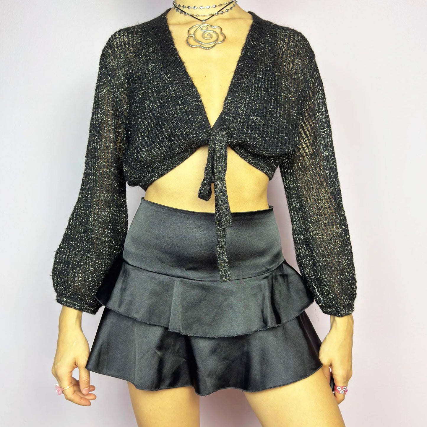 This Y2K Black Tie Front Cardigan is a vintage 2000s piece featuring a lightweight open-knit design with a subtle metallic shimmer, a cropped fit and long sleeves. Perfect for layering and ideal for night-out or casual outfits.