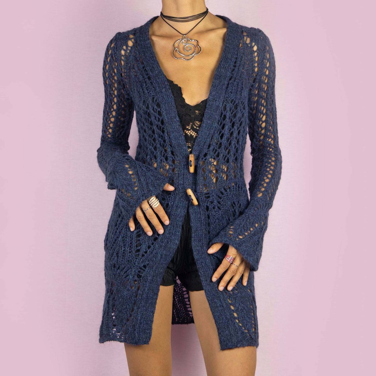 The Y2K Blue Long Crochet Cardigan is a vintage 2000s cardigan featuring a deep V-neckline and long, flared sleeves. Made from a wool blend, this longline cardigan is lightweight yet cozy, with wooden toggle button closures and a stretchy design. Perfect for layering over outfits in cooler weather.