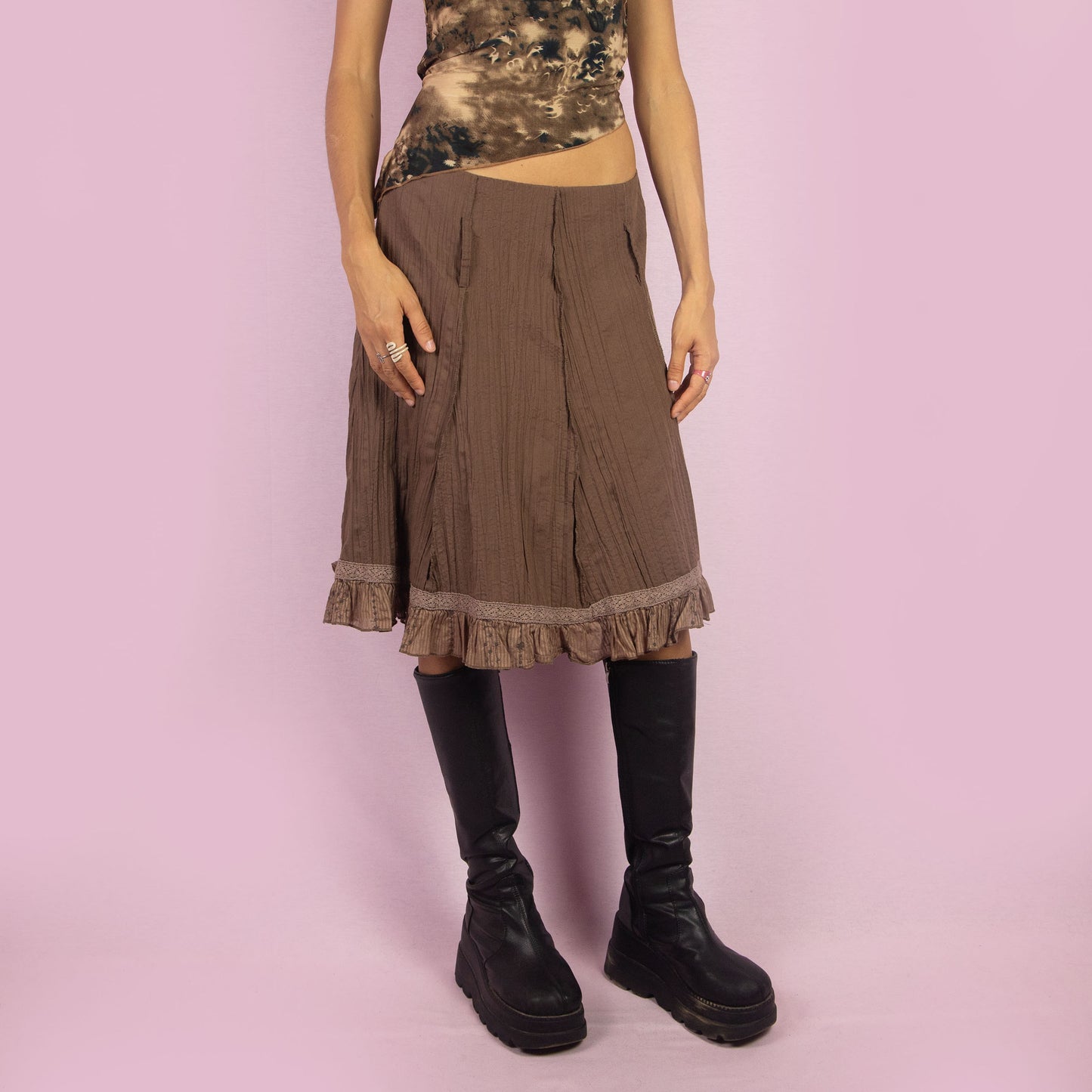 The Y2K Brown Flared Skirt is a vintage 2000s high-waisted skirt featuring a side zipper closure, a crinkled fabric texture, and delicate lace trim along the hemline with ruffle detailing. Perfect for casual or summer looks.