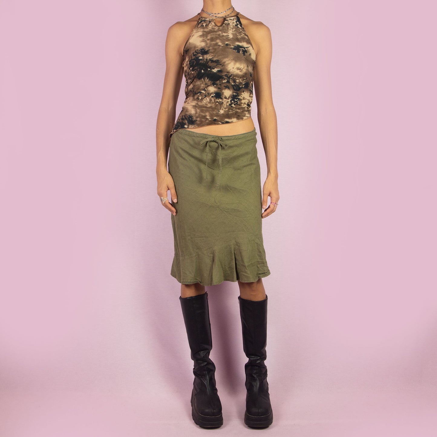 The Y2K Khaki Tie Waist Skirt is a vintage 2000s green mini skirt featuring a relaxed, high-waisted fit with a drawstring waist for adjustable styling. The skirt is finished with a subtle ruffle hem. Ideal for a casual summer look.