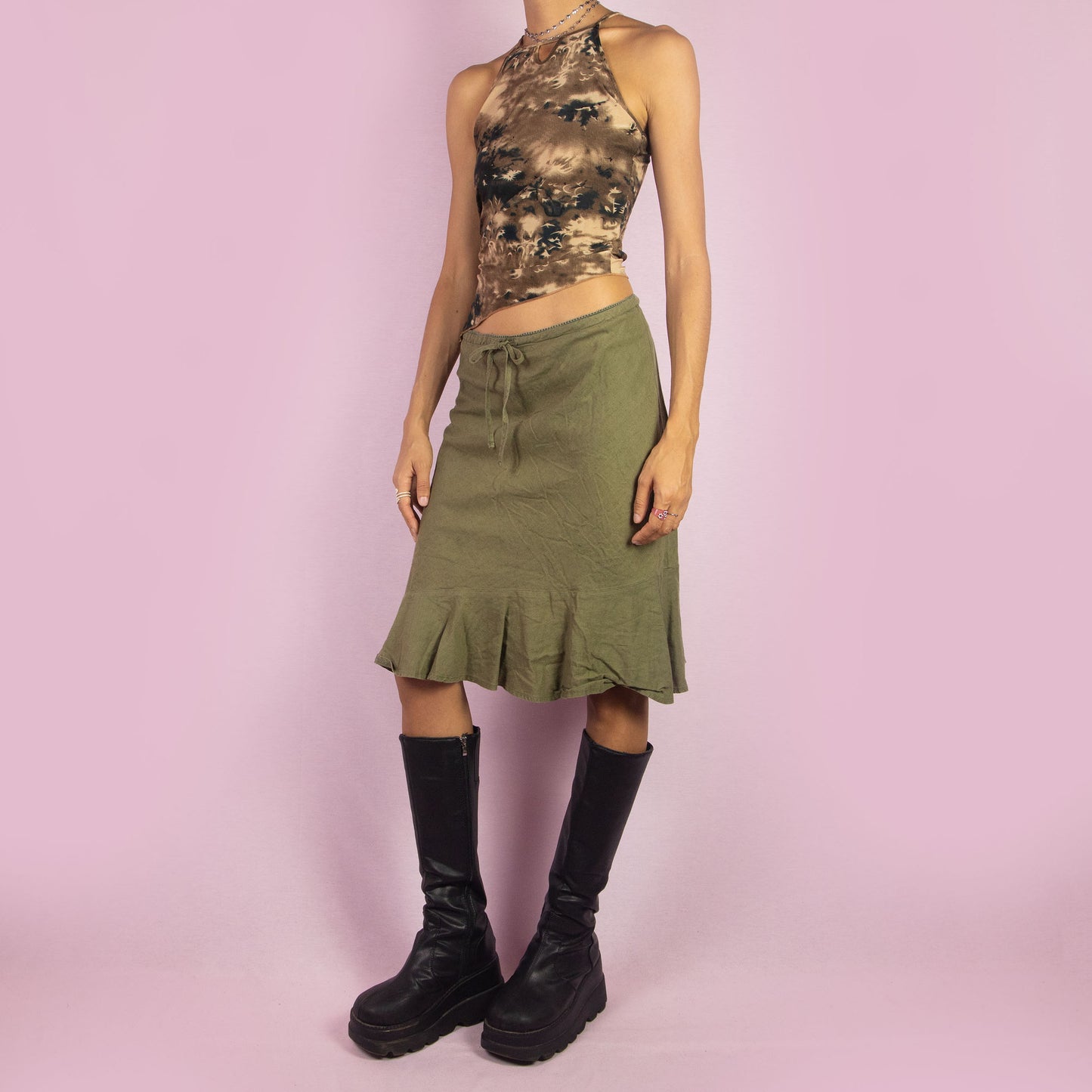 The Y2K Khaki Tie Waist Skirt is a vintage 2000s green mini skirt featuring a relaxed, high-waisted fit with a drawstring waist for adjustable styling. The skirt is finished with a subtle ruffle hem. Ideal for a casual summer look.