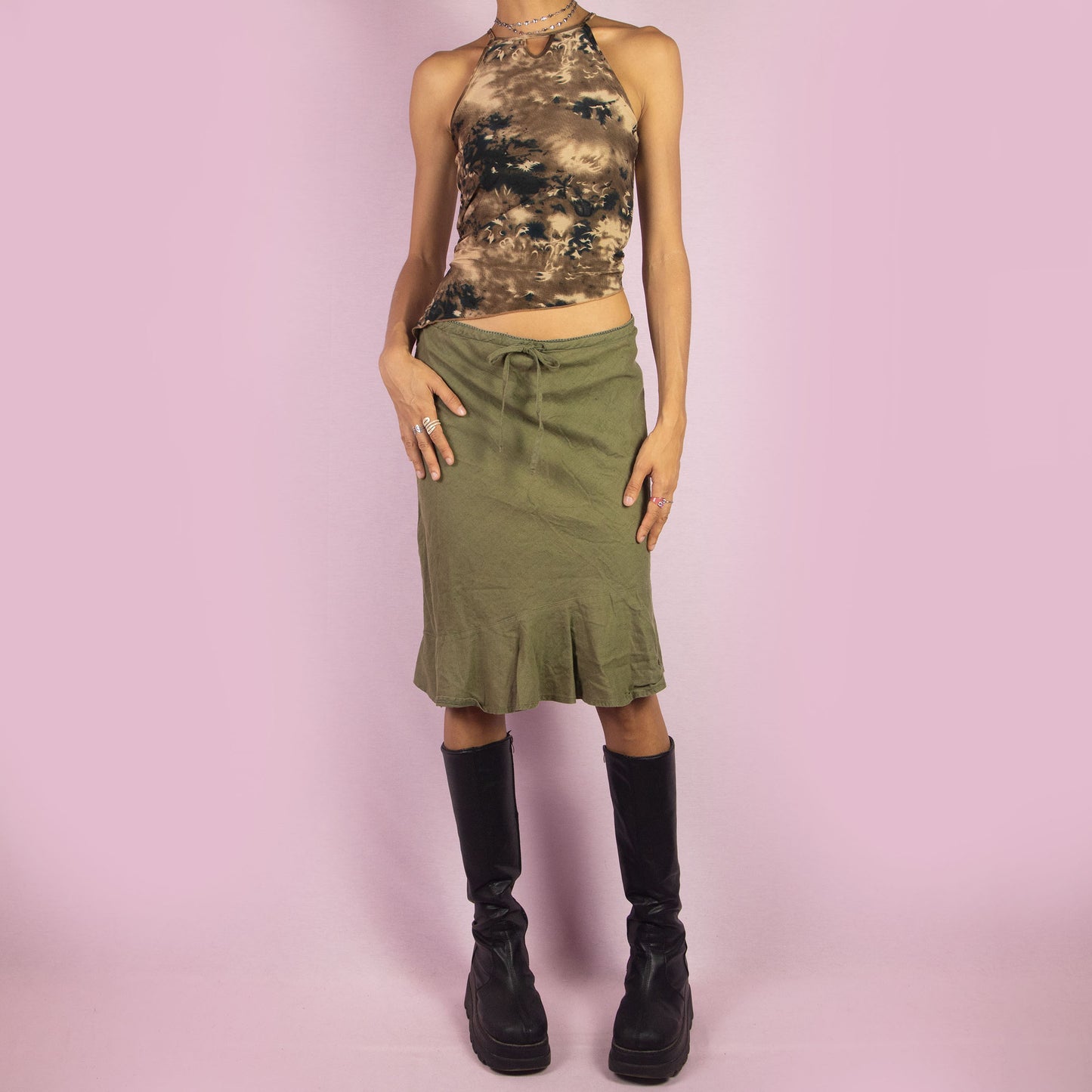 The Y2K Khaki Tie Waist Skirt is a vintage 2000s green mini skirt featuring a relaxed, high-waisted fit with a drawstring waist for adjustable styling. The skirt is finished with a subtle ruffle hem. Ideal for a casual summer look.