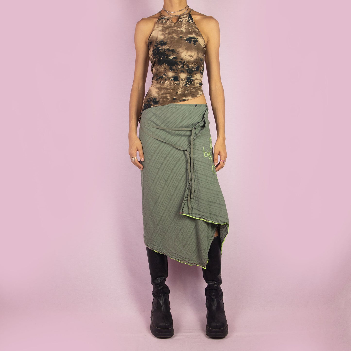 The Y2K Khaki Asymmetric Cop Copine Skirt is a unique vintage 2000s midi skirt showcasing the brand's signature avant-garde style. This high-waisted skirt features an asymmetrical hem and snap button detailing. Made with a lightweight fabric, it's an ideal choice for summer.
