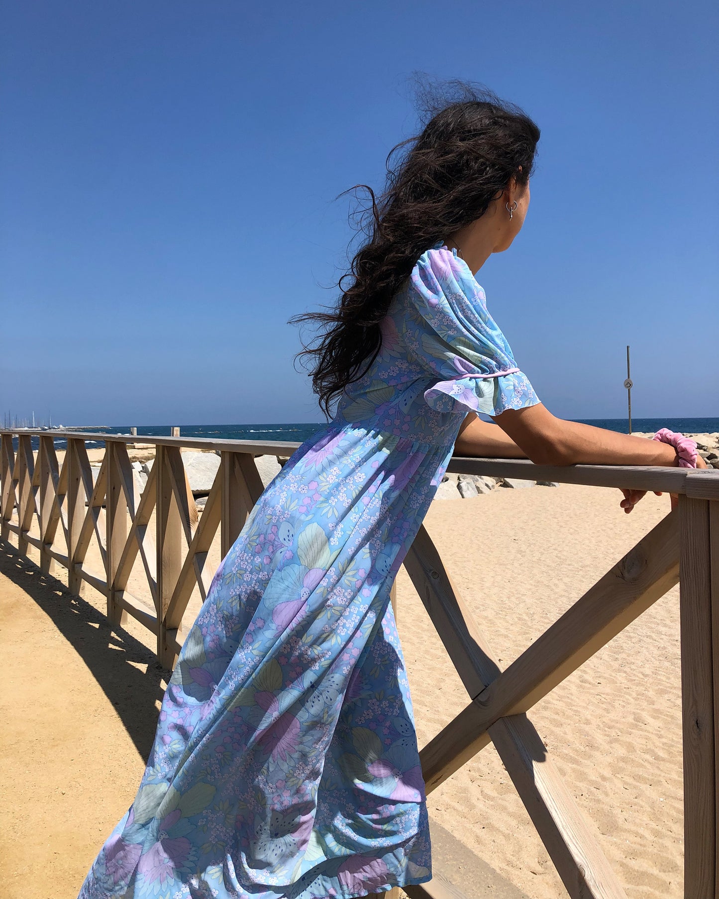 This vintage 1970s blue floral midi dress features lightweight semi-sheer fabric in soft pastel tones with a square neckline and ruffle trim, puff sleeves with frilled cuffs, and a button-front bodice. The empire waist and flowing length create gentle prairie romance for spring picnics, cottagecore styling, or feminine nostalgia. Made in France from a polyamide nylon blend. Excellent vintage condition.