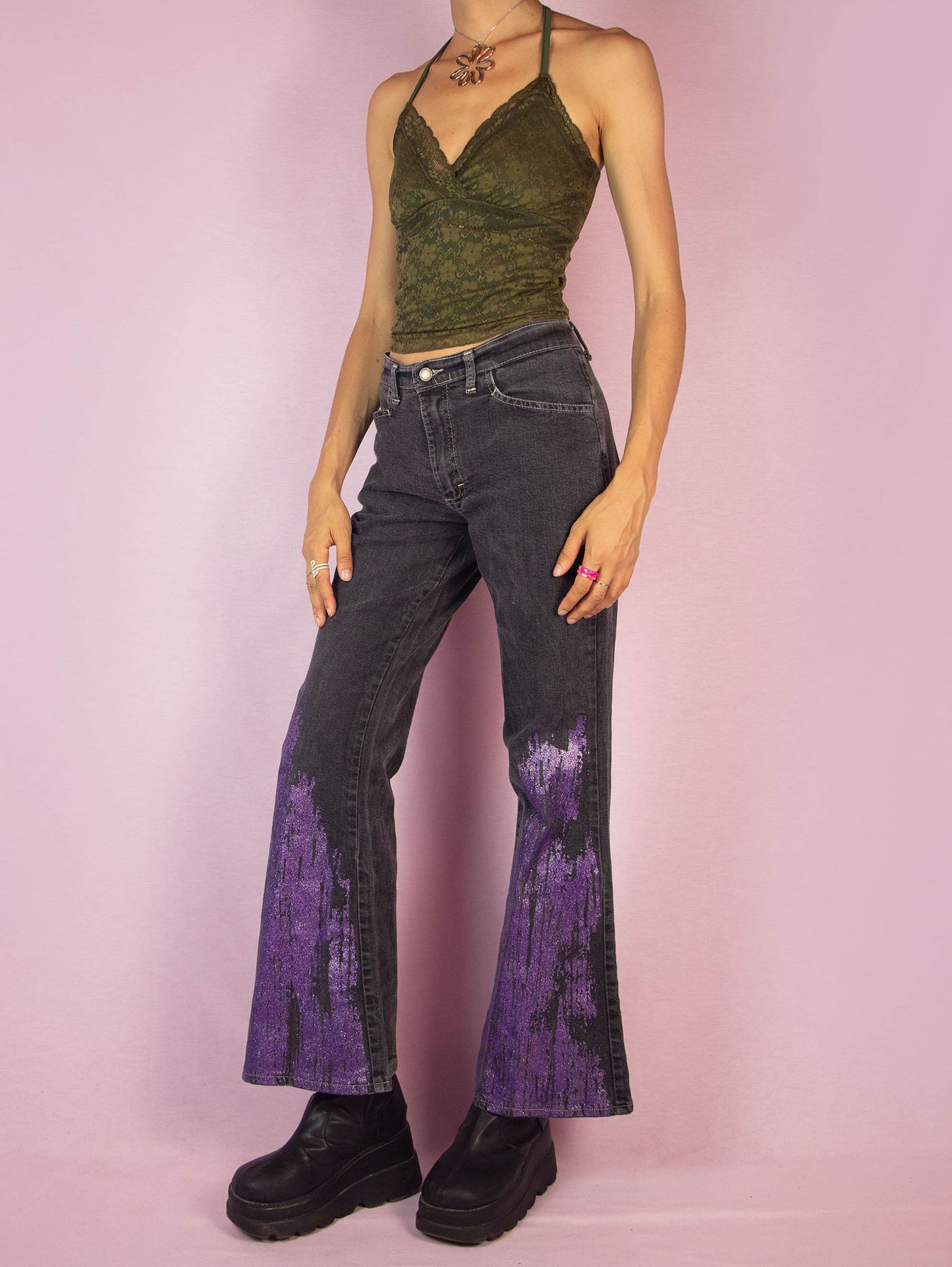 The Y2K Gray Flare Jeans are a vintage 2000s mid-rise pants featuring stretchy gray denim with purple glitter paint splatter detailing on the flared legs, front pockets, and a zipper closure. Perfect for festival looks or casual outfits. Made in UK.