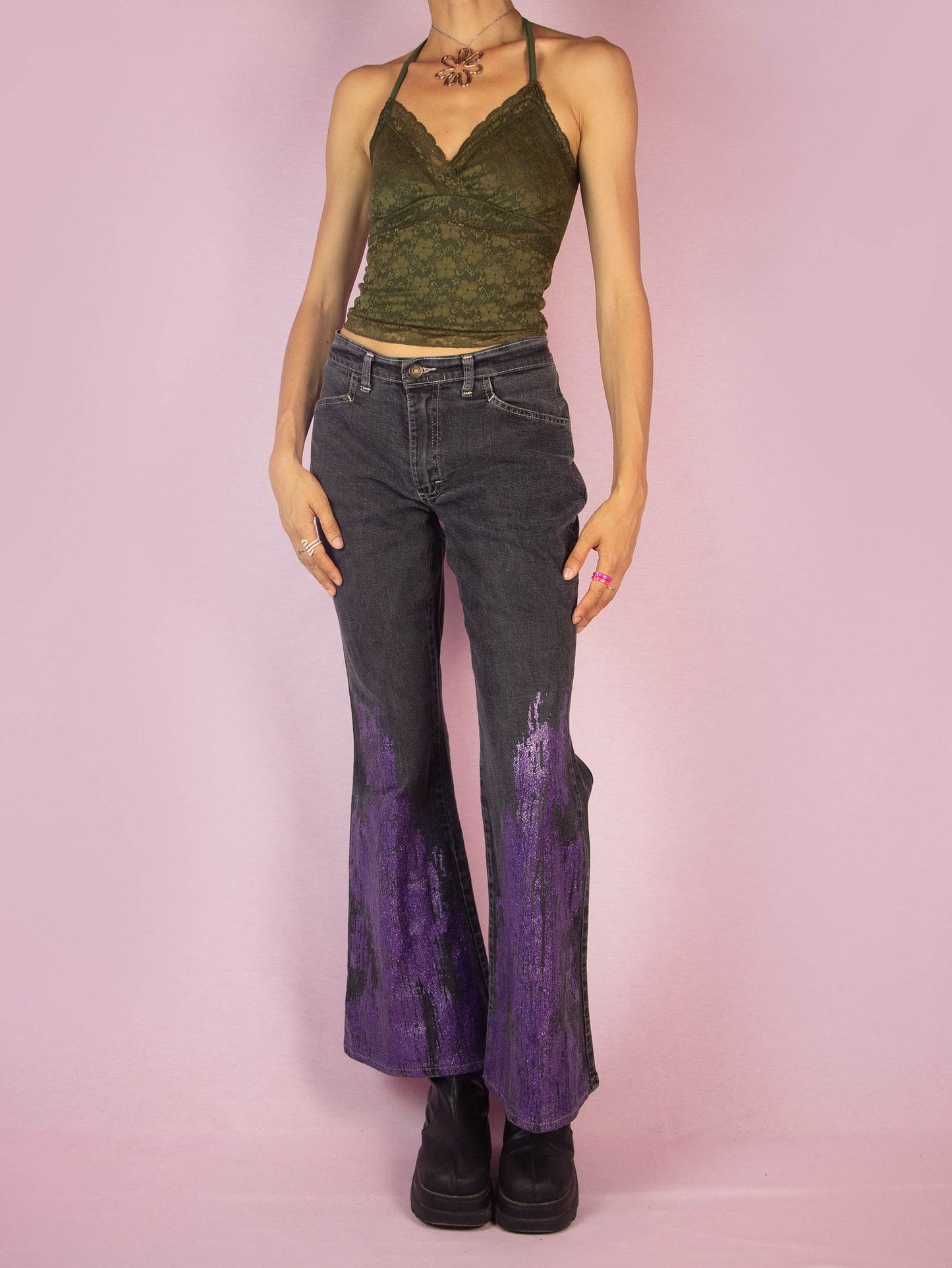 The Y2K Gray Flare Jeans are a vintage 2000s mid-rise pants featuring stretchy gray denim with purple glitter paint splatter detailing on the flared legs, front pockets, and a zipper closure. Perfect for festival looks or casual outfits. Made in UK.
