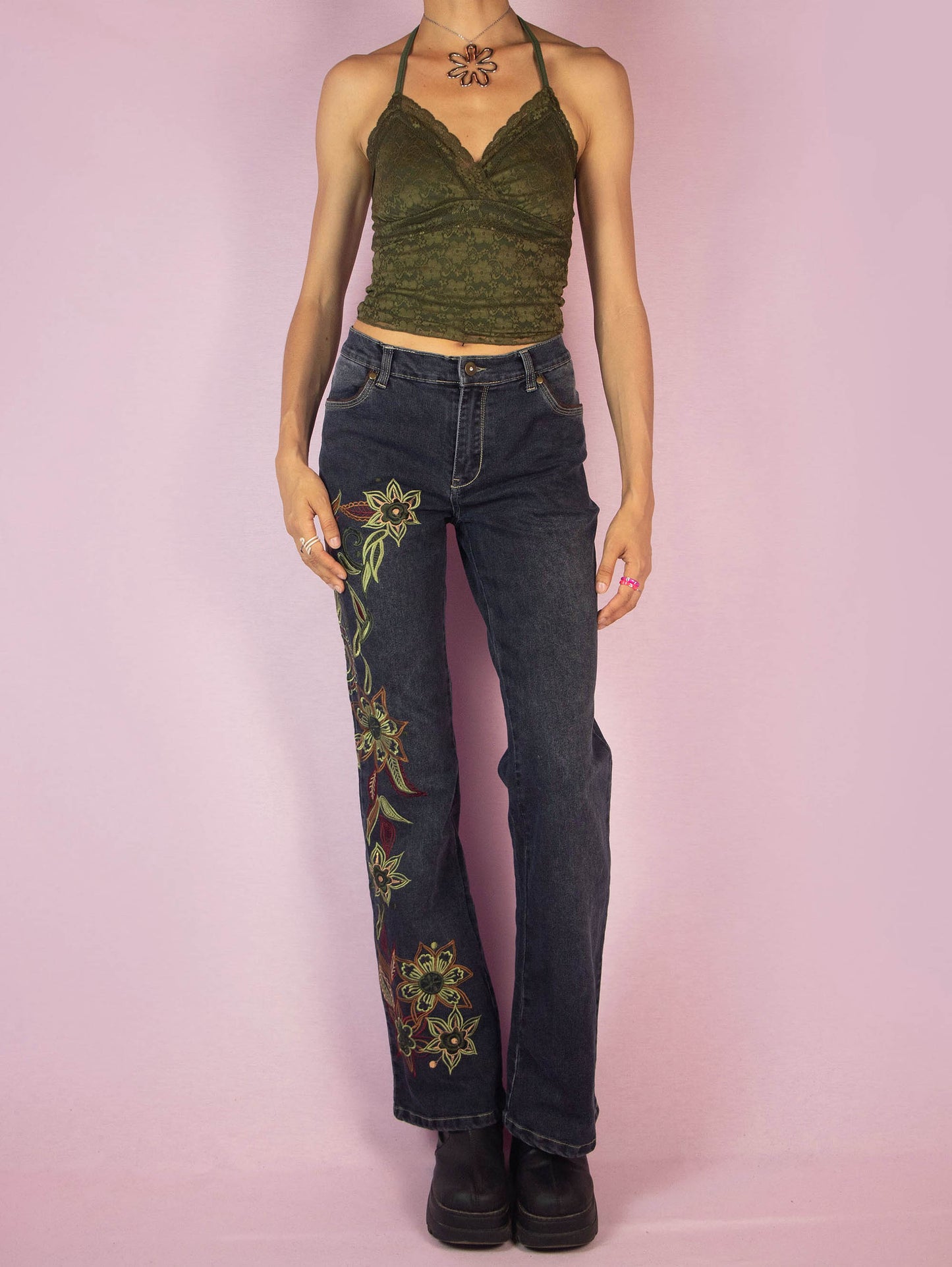 The Y2K Floral Embroidered Jeans are a vintage 2000s piece featuring floral embroidery along the leg, a mid-rise fit, stretchy dark denim, straight leg cut, front and back pockets, and a zipper closure. These jeans add a unique, bohemian flair to your casual or festival outfits.