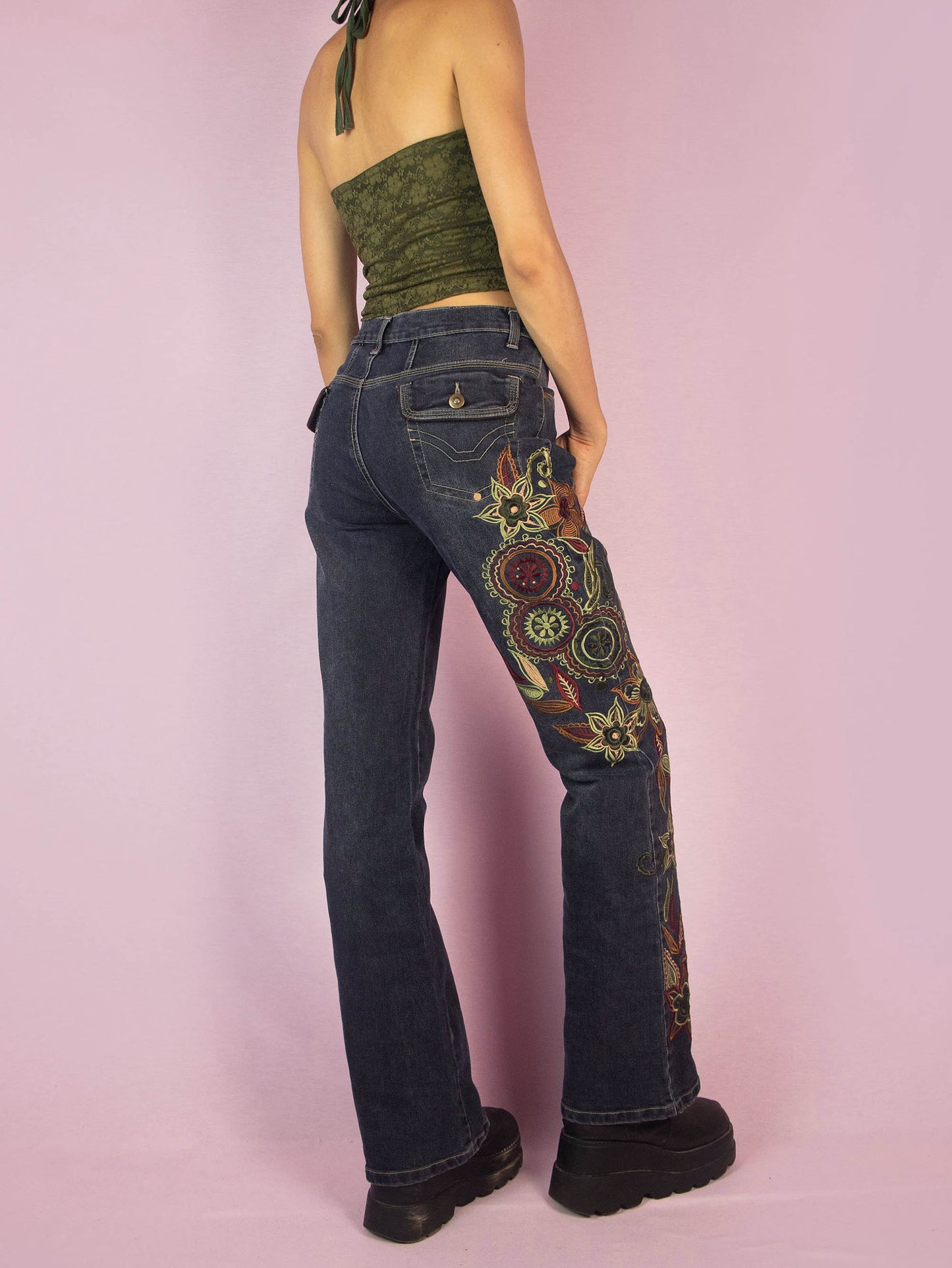 The Y2K Floral Embroidered Jeans are a vintage 2000s piece featuring floral embroidery along the leg, a mid-rise fit, stretchy dark denim, straight leg cut, front and back pockets, and a zipper closure. These jeans add a unique, bohemian flair to your casual or festival outfits.
