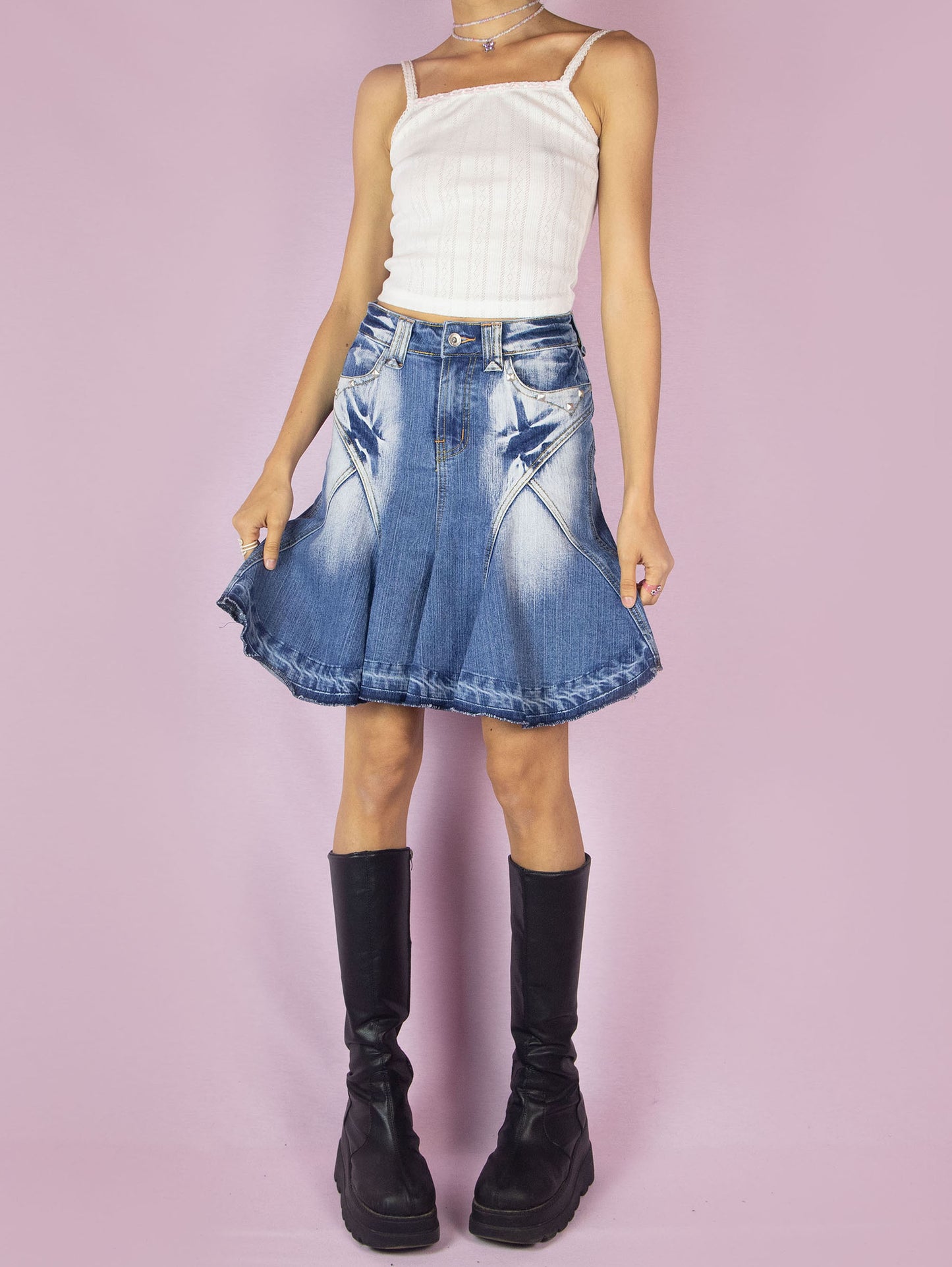 The Y2K Denim Godet Trumpet Skirt is a vintage 2000s subversive deconstructed inspired jean mini skirt featuring acid wash and stud details, a raw hem, pockets, and a front zipper closure.