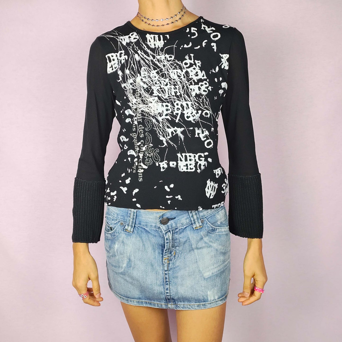 The Y2K Black Printed Top is a vintage 2000s piece with an abstract white graphic print throughout the front. This stretchy top features a sleek black base, flared mesh sleeves, and extended knit cuffs. Ideal for casual wear or a night-out ensemble.