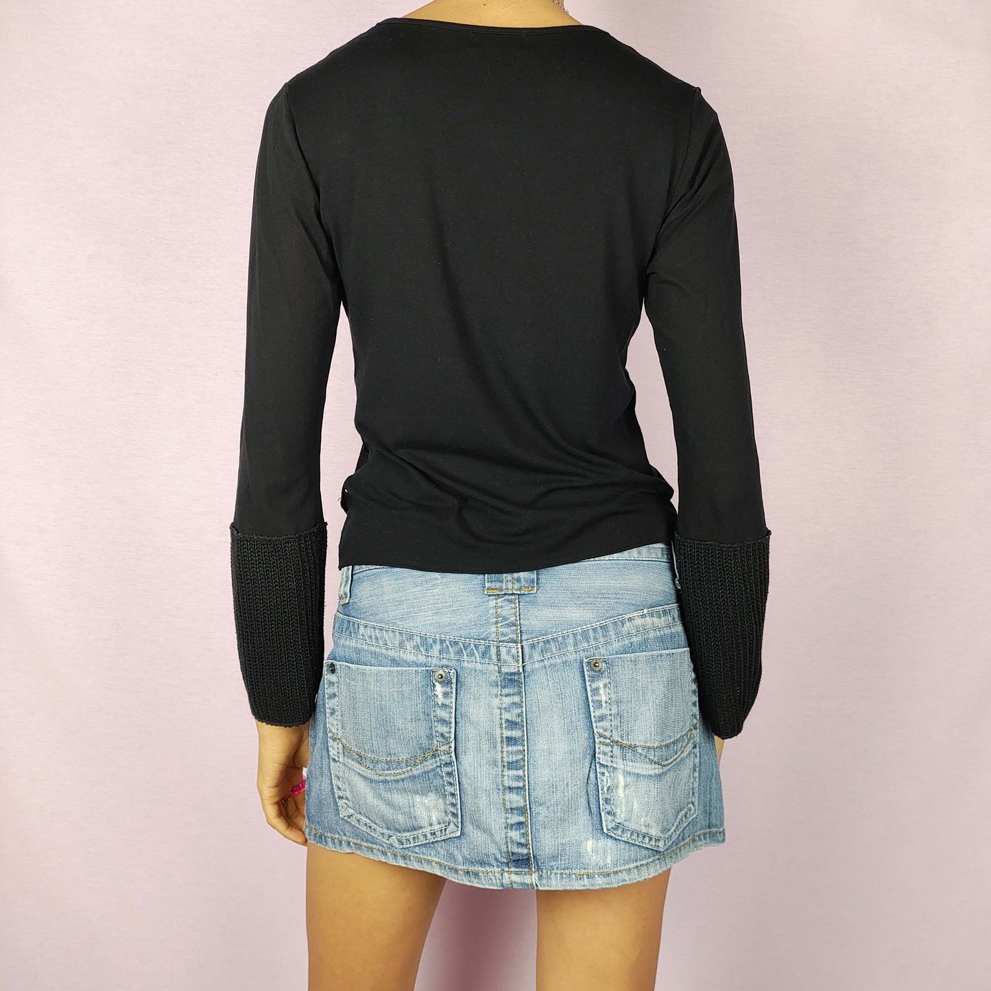 The Y2K Black Printed Top is a vintage 2000s piece with an abstract white graphic print throughout the front. This stretchy top features a sleek black base, flared mesh sleeves, and extended knit cuffs. Ideal for casual wear or a night-out ensemble.