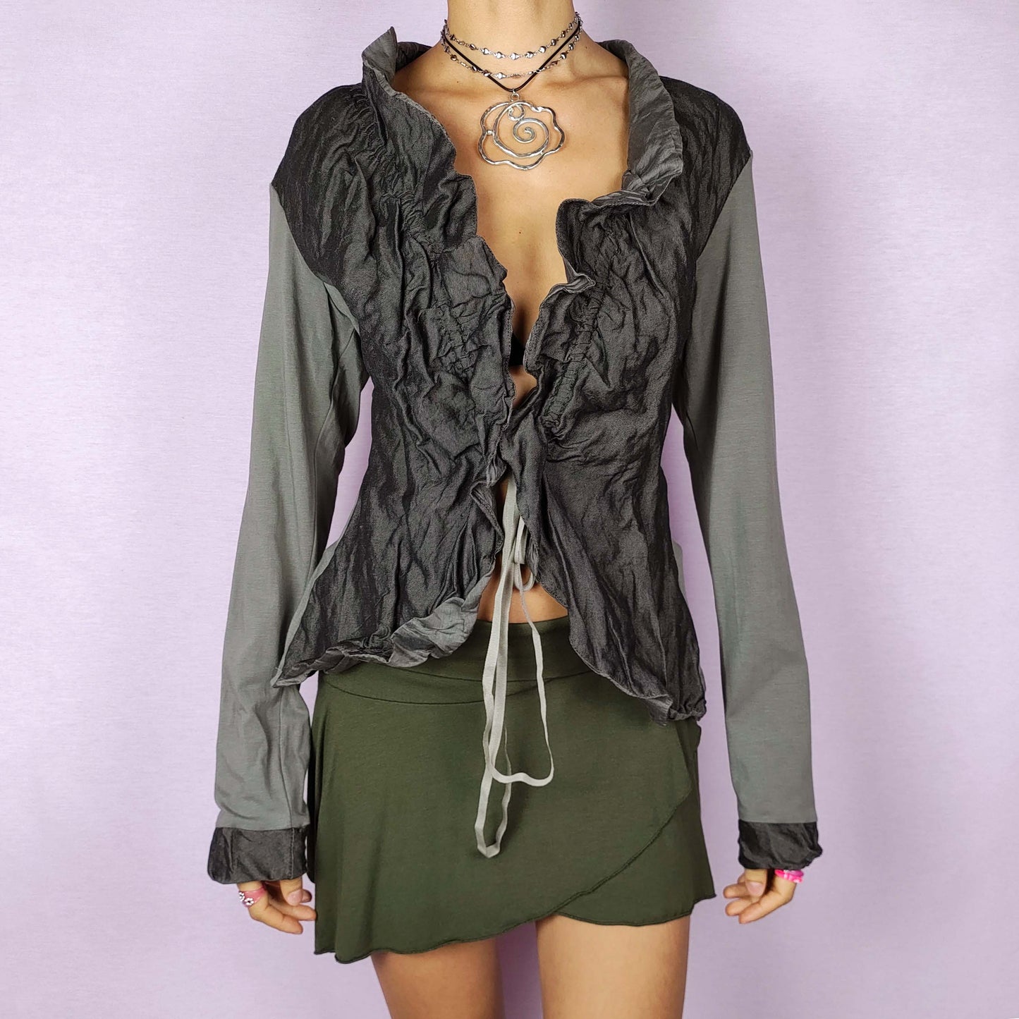 The Y2K Ruffle Tie Front Top is a vintage 2000s khaki-green grayish elegant and formal bolero jacket featuring a unique crinkled texture, ruffled details along the front and an adjustable tie closure. Perfect for both office wear and evening events.