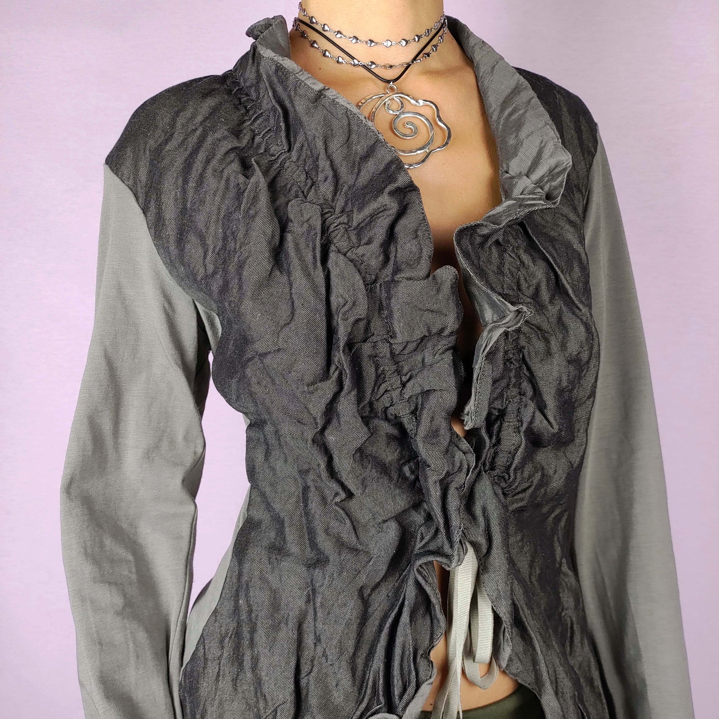 The Y2K Ruffle Tie Front Top is a vintage 2000s khaki-green grayish elegant and formal bolero jacket featuring a unique crinkled texture, ruffled details along the front and an adjustable tie closure. Perfect for both office wear and evening events.