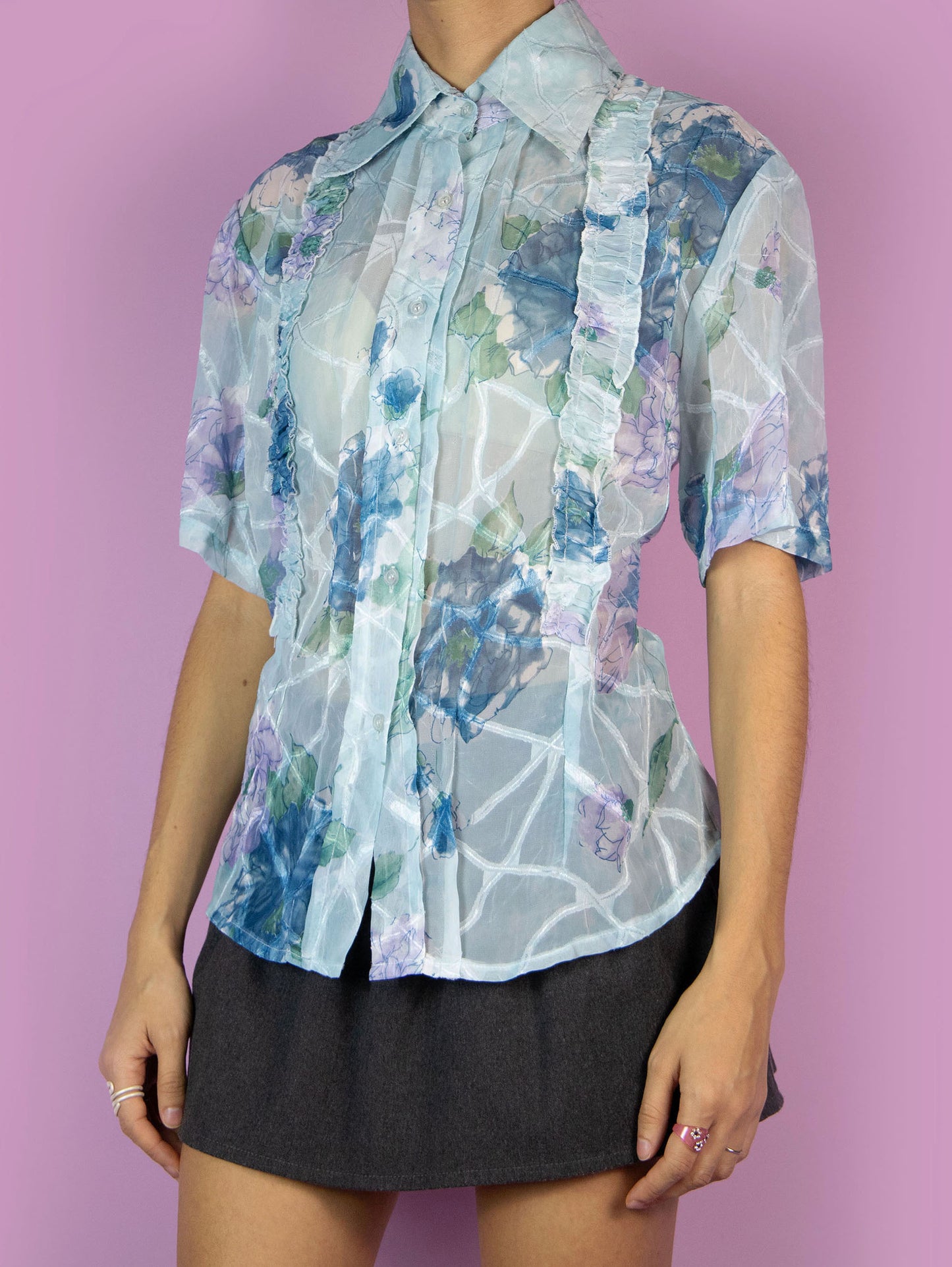 The Y2K Print Sheer Blouse is a vintage 2000s boho summer style light blue floral graphic semi-transparent short-sleeve top with a collar, buttons, and gathered ruffle details.