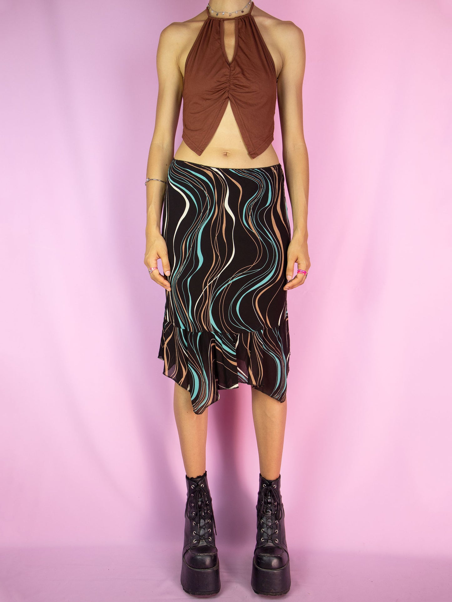 The Y2K Brown Print Trumpet Skirt is a vintage 2000s midi skirt that features an abstract wavy pattern in multicolor shades on a dark brown background, an asymmetric hemline with pointed edges and ruffle details, as well as an elastic waistband. Perfect for casual outings and summer events.