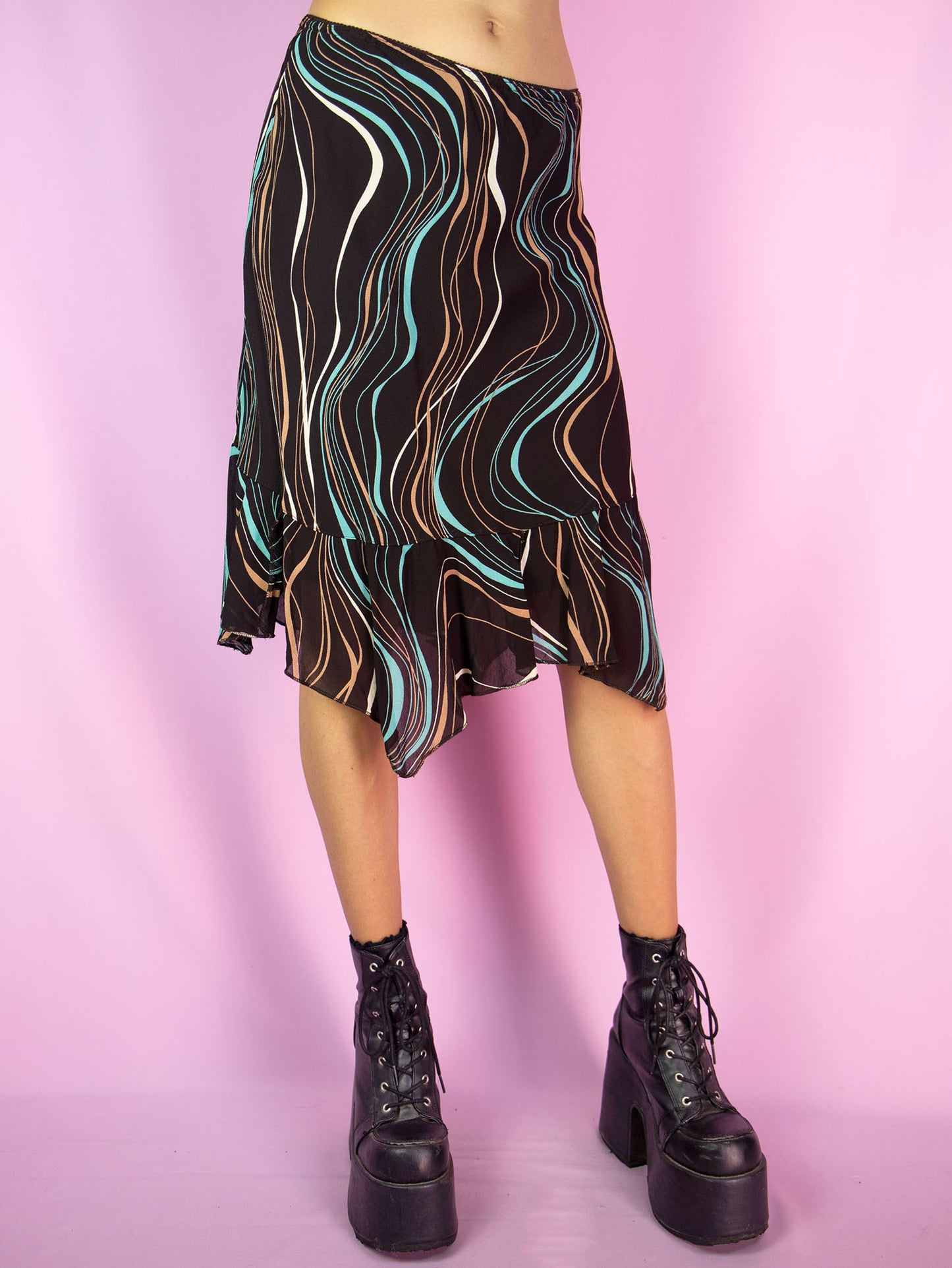 The Y2K Brown Print Trumpet Skirt is a vintage 2000s midi skirt that features an abstract wavy pattern in multicolor shades on a dark brown background, an asymmetric hemline with pointed edges and ruffle details, as well as an elastic waistband. Perfect for casual outings and summer events.