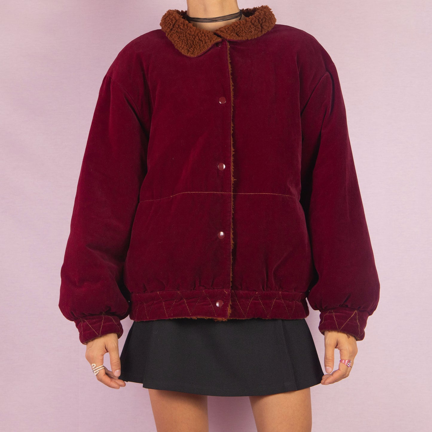 The Vintage 90s Red Velvet Bomber Jacket is a striking piece with a deep red velvet exterior featuring a contrasting brown faux shearling collar and inner lining. It includes snap button closures. Perfect for casual winter days or adding a bold touch to any outfit. Made in Italy.