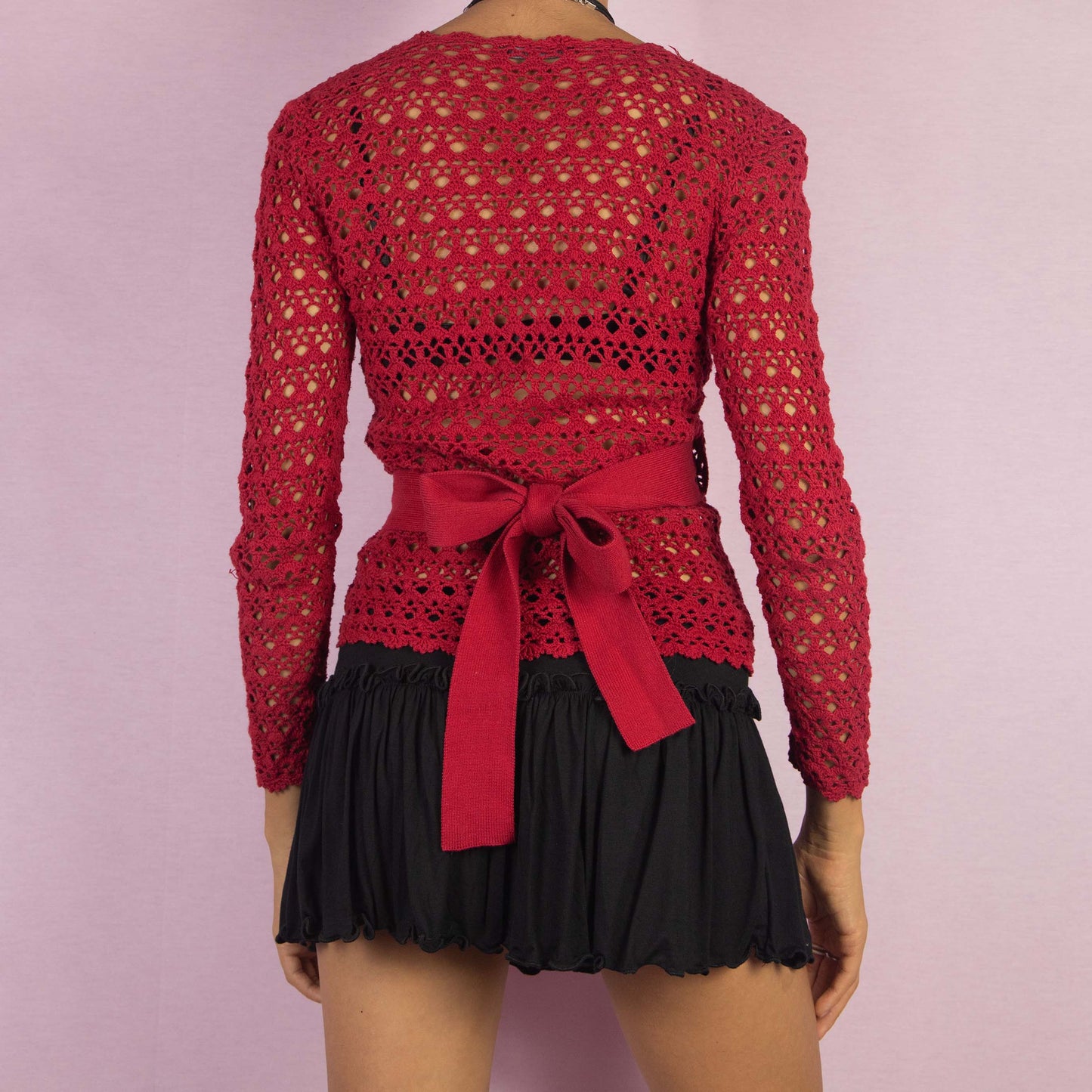The Y2K Red Crochet Wrap Cardigan is a vintage 2000s piece featuring a romantic deep V-neckline with an intricate open-knit design. Its wrap style and tie closure at the back form a stylish bow, creating a flattering silhouette. Perfect for layering in spring and summer.