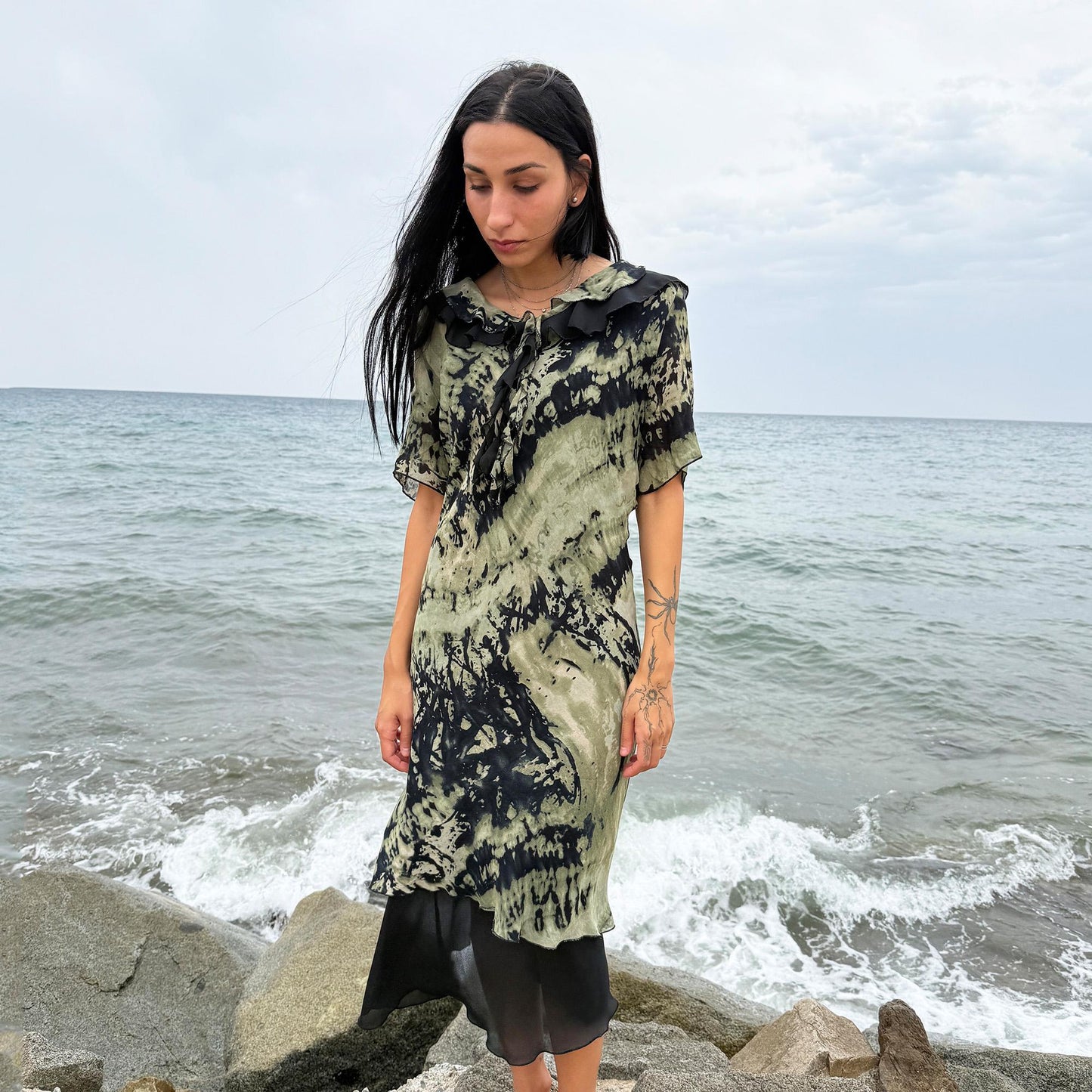 This vintage 90s midi dress features a black and green tie-dye pattern with a ruffled neckline. The short sleeves and flowy layered hem make it ideal for summer festivals, boho gatherings, or dark fairy-inspired looks. A unique Italian-made piece, perfect for forest parties or artistic styling. Made in Italy from lightweight non-stretch fabric. Excellent vintage condition.