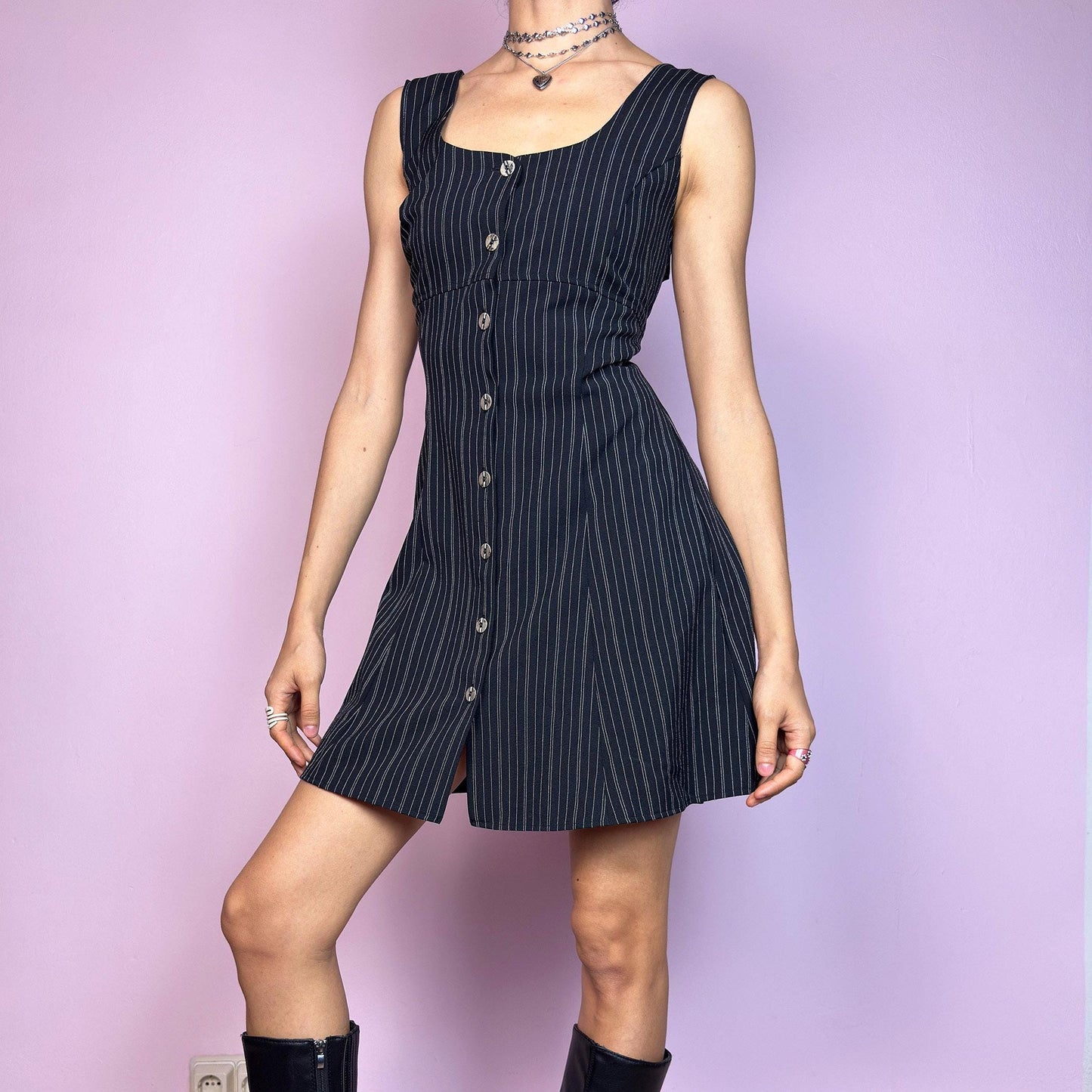 The Vintage 90s Black Pinstripe Mini Dress is a timeless piece with a flirty twist. This sleeveless dress features a black base with fine pinstripes, a fitted bodice with a square neckline, and a full front button closure. The slight A-line silhouette flatters the waist while keeping the vibe playful and polished. Ideal for 90s office-core and preppy looks. Excellent vintage condition.