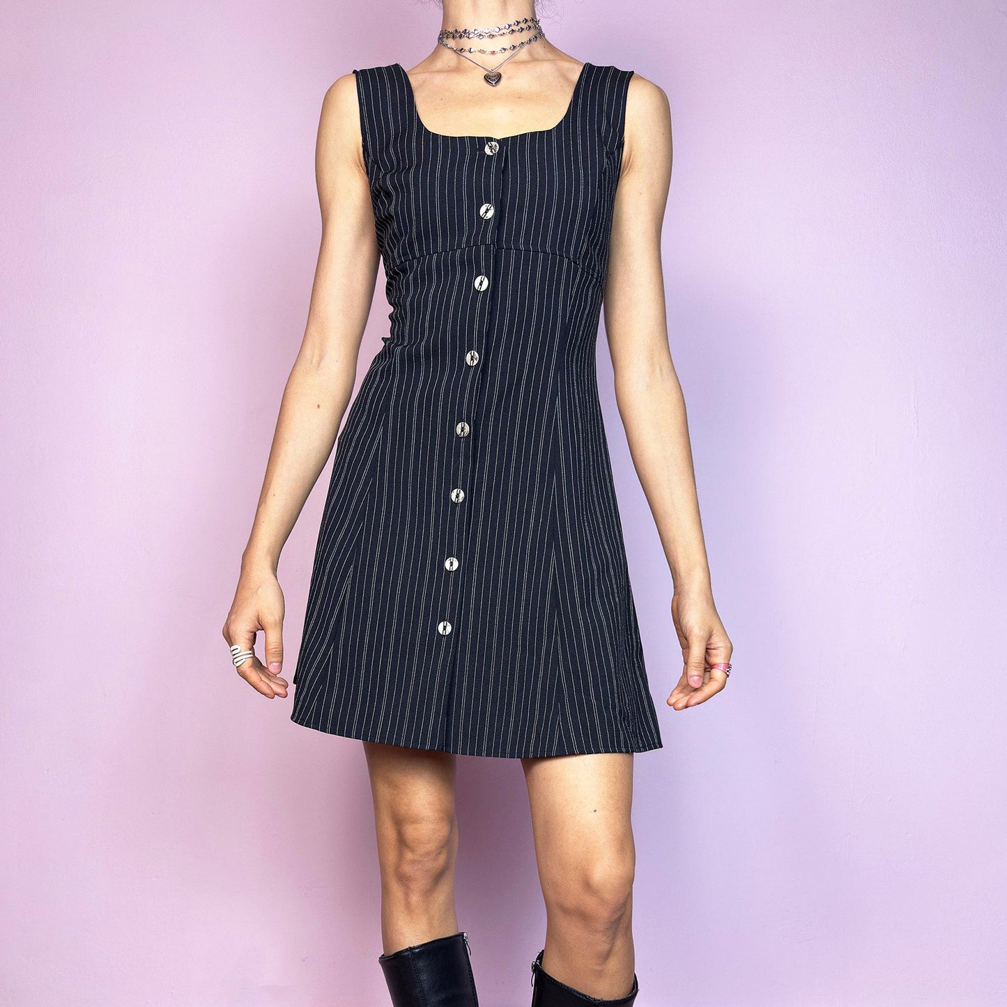 The Vintage 90s Black Pinstripe Mini Dress is a timeless piece with a flirty twist. This sleeveless dress features a black base with fine pinstripes, a fitted bodice with a square neckline, and a full front button closure. The slight A-line silhouette flatters the waist while keeping the vibe playful and polished. Ideal for 90s office-core and preppy looks. Excellent vintage condition.