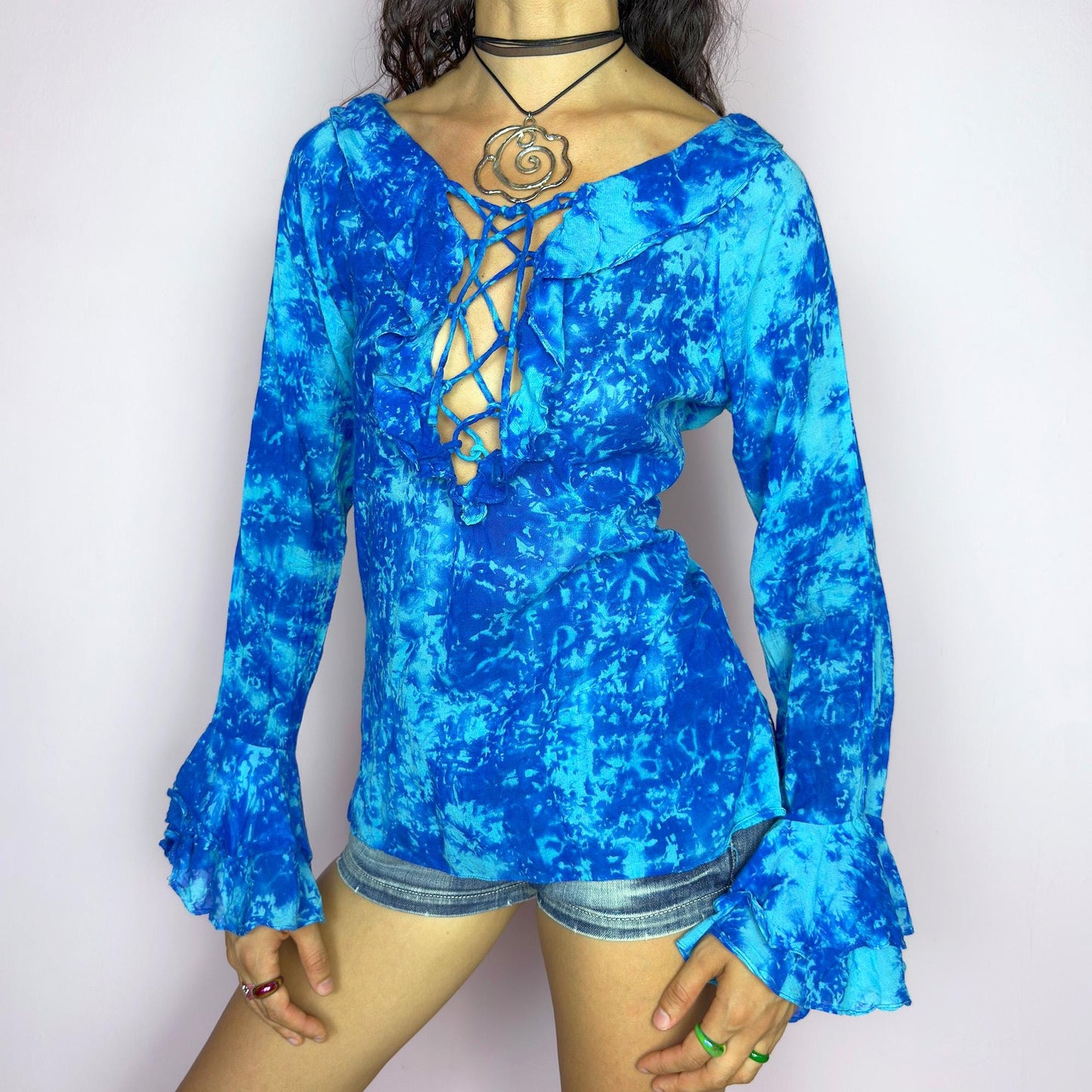 This vintage 90s blue tie dye top features dramatic ruffle cuffs, a deep lace-up neckline, and soft cotton-blend fabric in vibrant psychedelic tones. Designed with long sleeves it channels boho, hippie, and festival energy with bold originality. Lightweight and breathable, perfect for summer layering or statement styling. A rare archival blouse that captures wild 90s freedom. Excellent vintage condition.