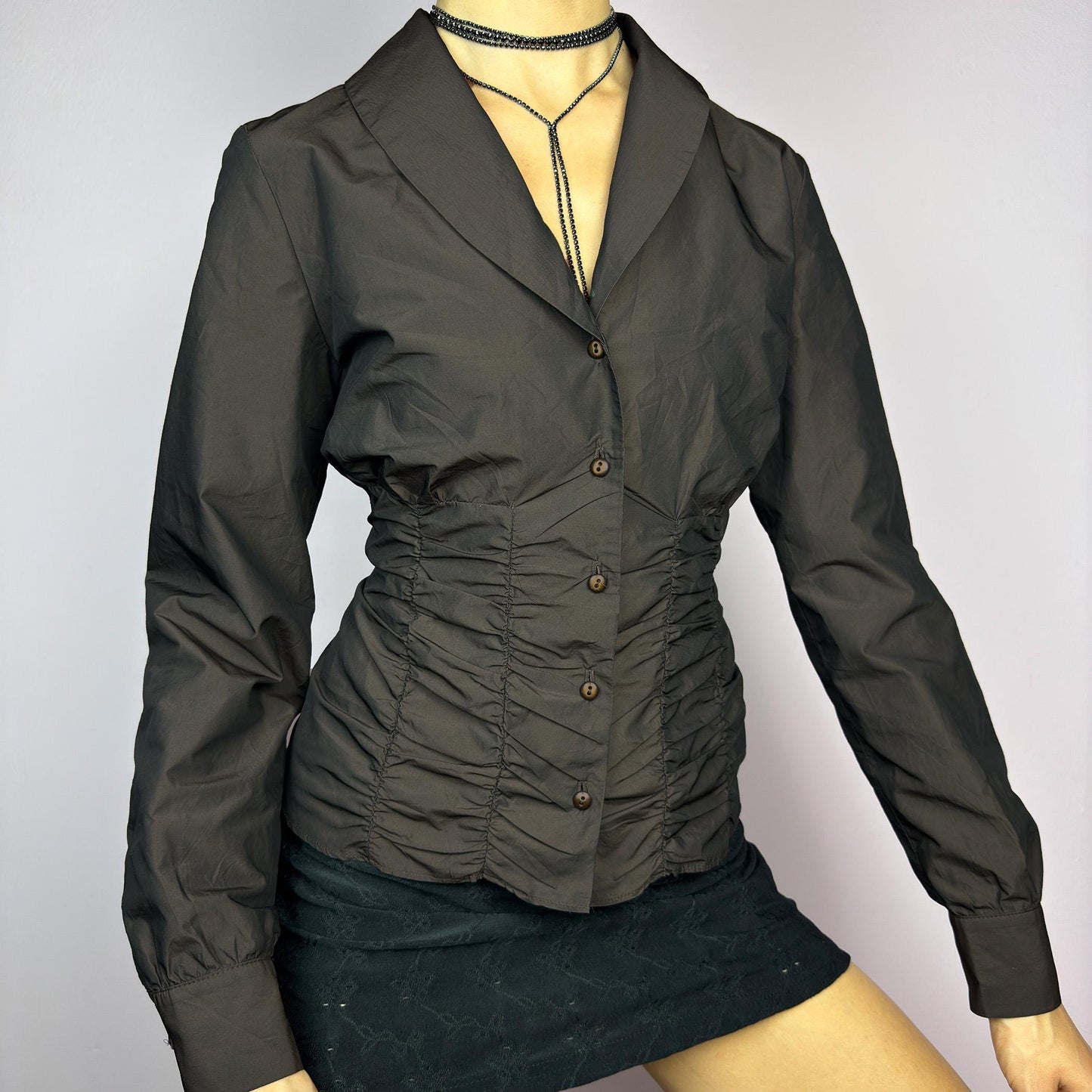 The Vintage 90s Brown Ruched Blouse features a structured yet feminine design with ruched detailing on both the front and back, creating a flattering silhouette. Crafted in a deep brown tone, it includes a tailored collar. adult world shop