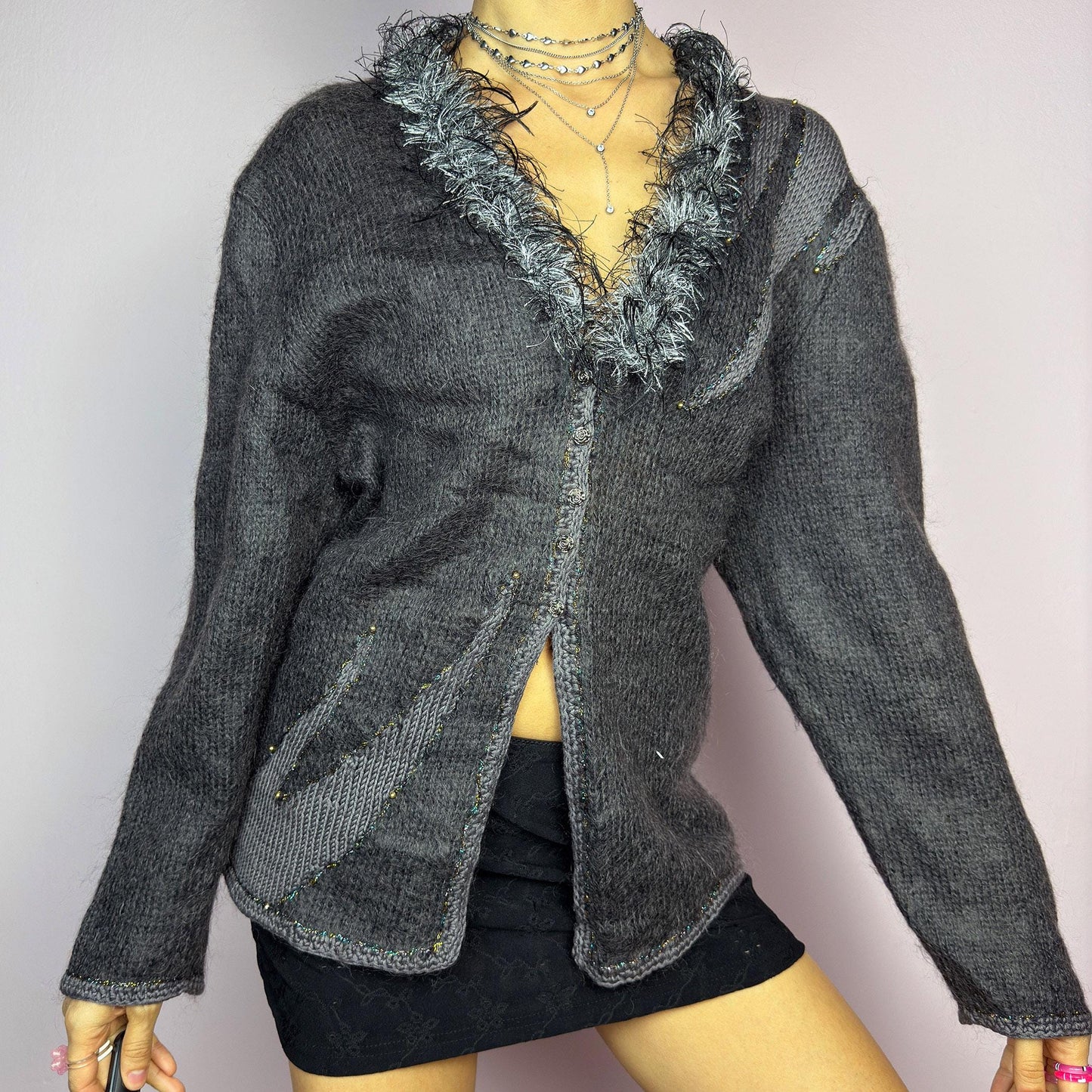 The Vintage 90s Gray Shaggy Trim Cardigan is a unique statement knitwear piece, featuring a soft knit fabric. Designed with a shaggy, hairy-textured trim along the V-neckline, subtle beaded embellishments, and button closure, this cardigan is perfect for cozy winter outfits. adult world shop