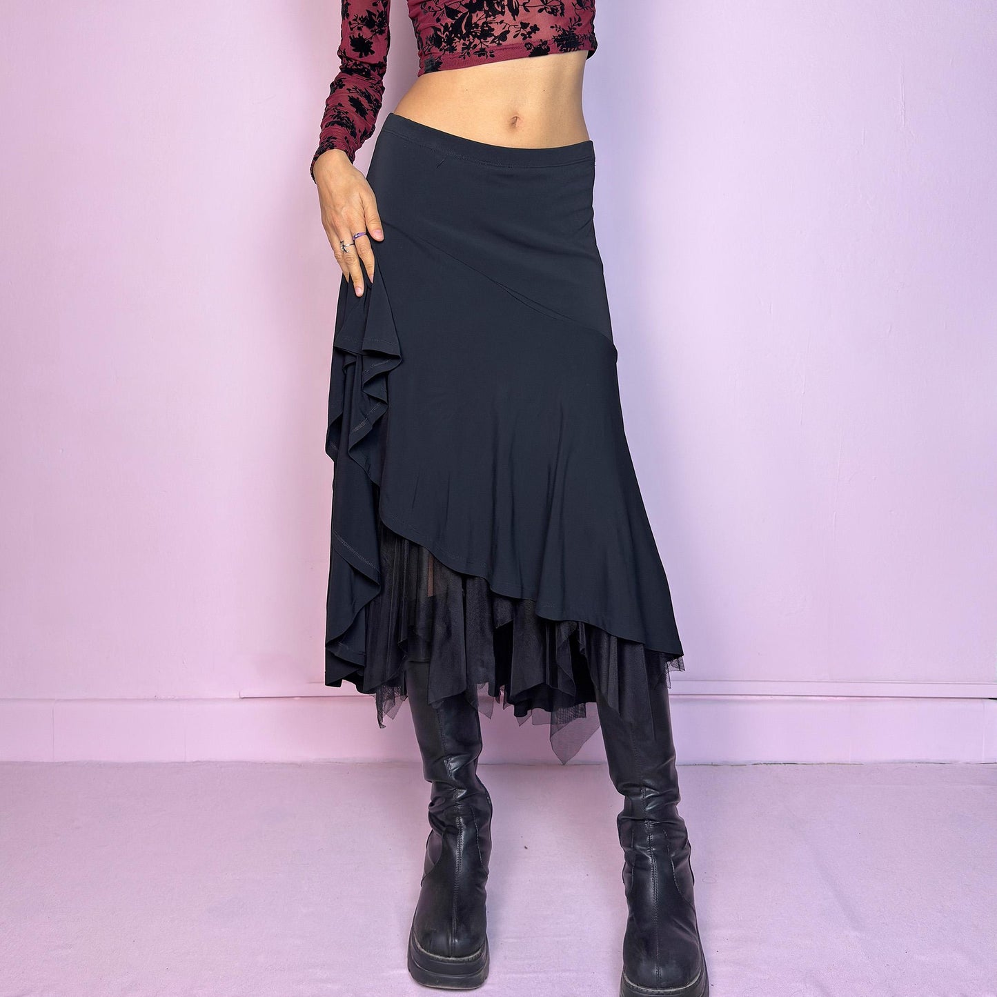 The Vintage 90s Layered Black Midi Skirt features a layered design with an asymmetrical hemline and a delicate tulle underlayer and an elastic waist. The trumpet silhouette enhances the figure, creating a dramatic and elegant flair. Adult World Shop