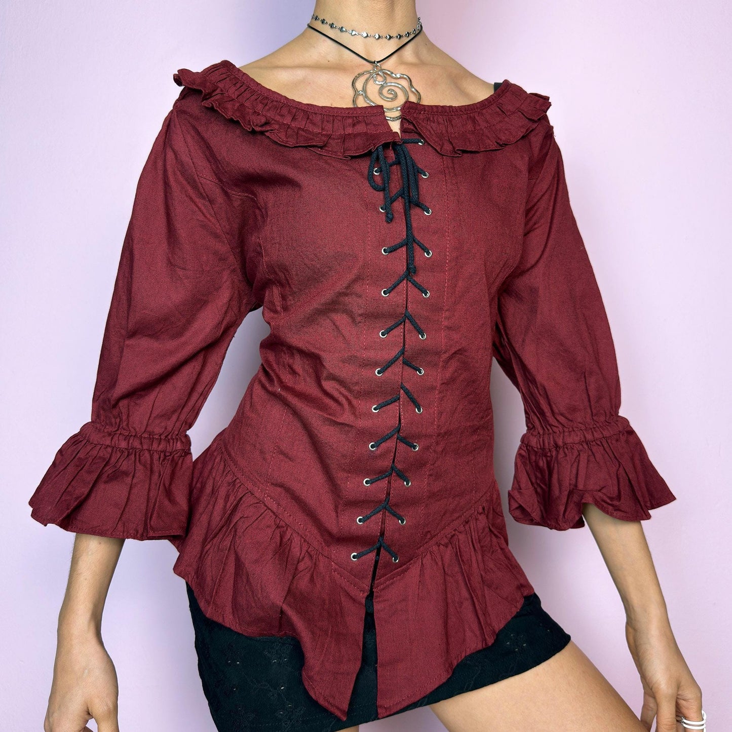 The Vintage 90s Maroon Lace Up Top is a romantic and dramatic piece inspired by gothic and cottagecore aesthetics. Crafted in a deep wine red tone, it features front and back corset-style lace-up details for an adjustable fit. The design includes a ruffled off-the-shoulder neckline, voluminous three-quarter sleeves with gathered ruffle cuffs, and a flattering cinched waist with a ruffled hem. Perfect for creating fairytale-inspired outfits or statement festival looks. adult world shop