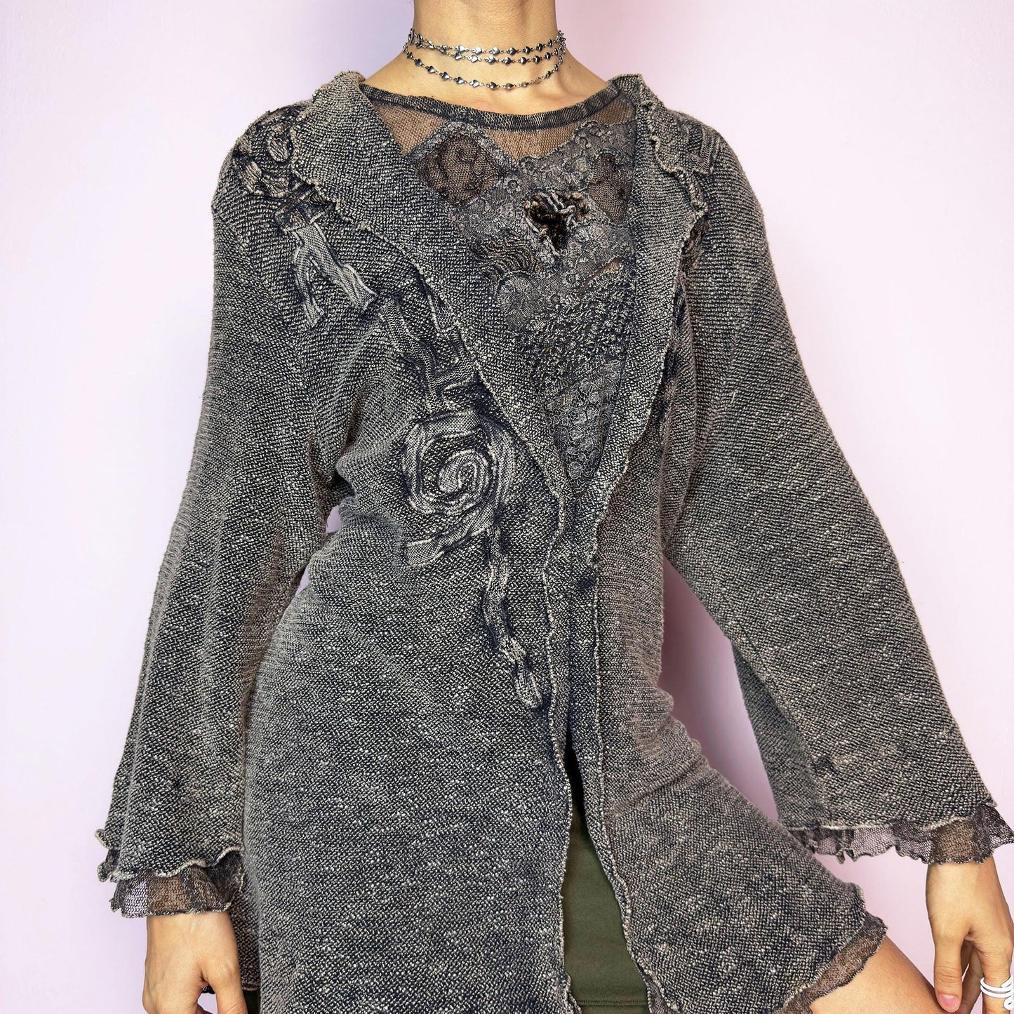 The Vintage 90s Medieval Ruffle Knit Top is a rare and enchanting piece with rustic, fairycore charm. Made from thick textured knit in a washed charcoal hue, it features flared three-quarter sleeves, ruffled lace trim, and intricate appliqué embroidery details. The open split front and ruffled hem bring a dramatic, medieval-inspired silhouette. Perfect for layering with romantic, witchy, or dark cottagecore outfits. Made in Italy. Great vintage condition.