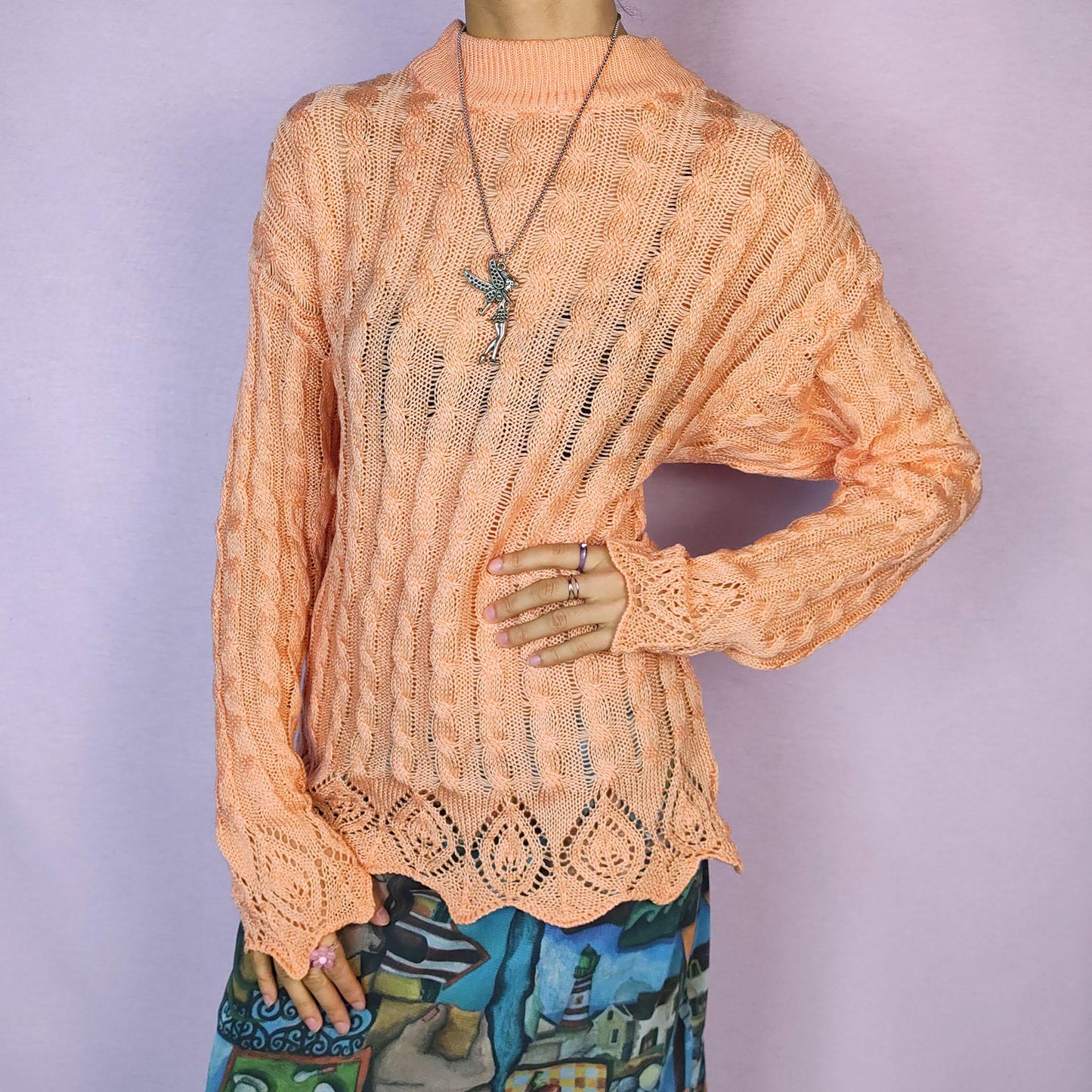 The Vintage 90s Peach Knit Sweater features a soft knit design with an openwork cable pattern, delicate scalloped hem detailing, long sleeves and a mock neckline. This lightweight sweater is crafted in a warm peach tone. Adult World Shop.