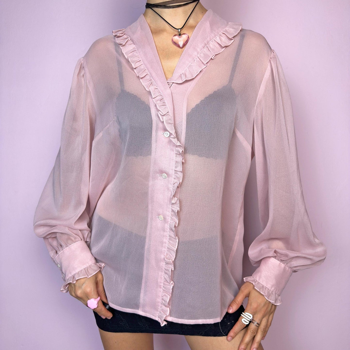 The Vintage Pink Ruffle Sheer Blouse features a romantic and ethereal silhouette with soft, see-through fabric and delicate ruffle trim along the collar and button placket. The flowy cut and voluminous sleeves with buttoned cuffs add a dreamy charm. Perfect for layering for a soft coquette aesthetic. Made in France. Excellent vintage condition. adult world shop