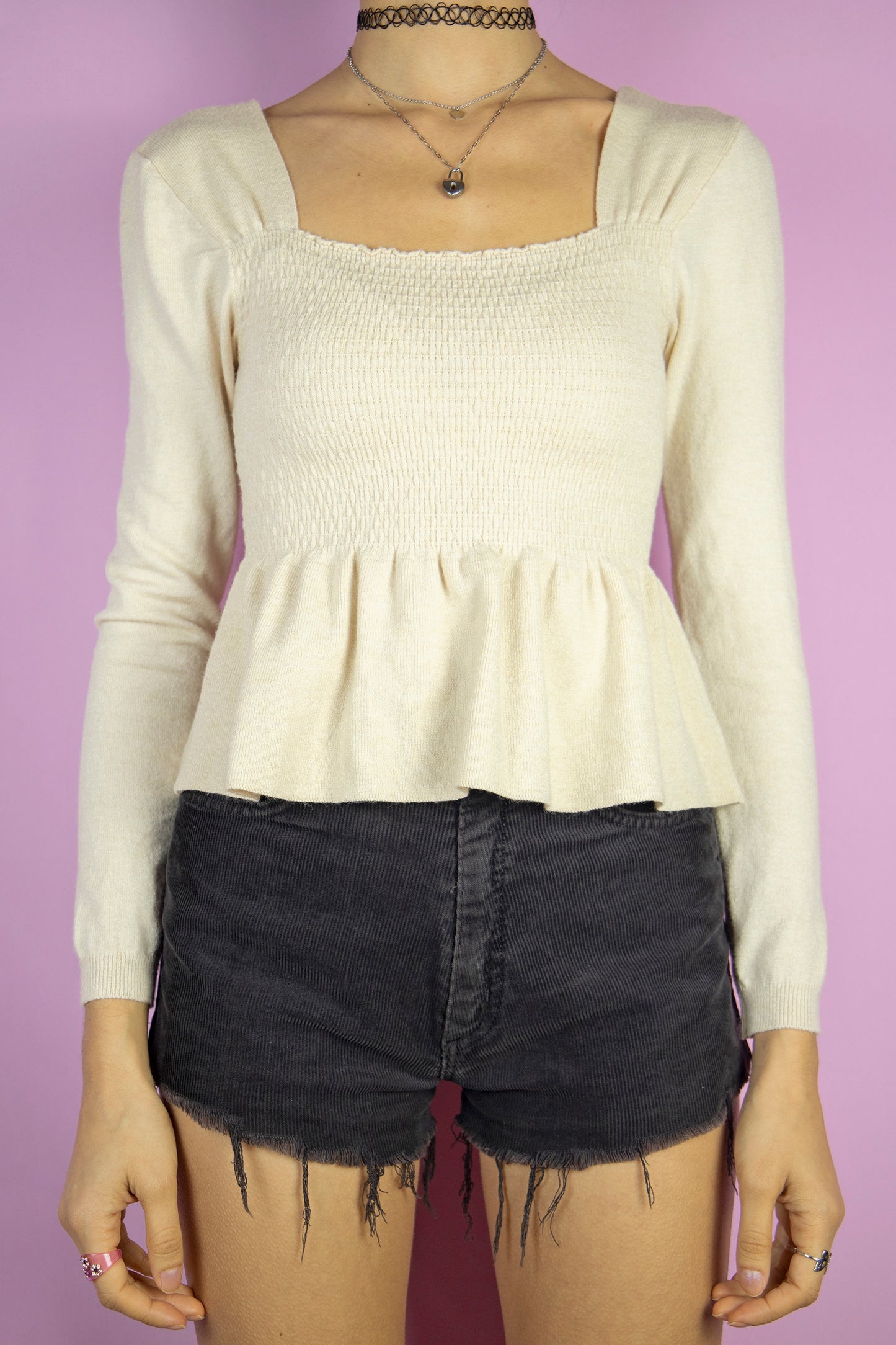 The Y2K Beige Shirred Peplum Top is a vintage 2000s knit blouse featuring a square neckline, long sleeves, and a shirred bodice that flows into a peplum hem.