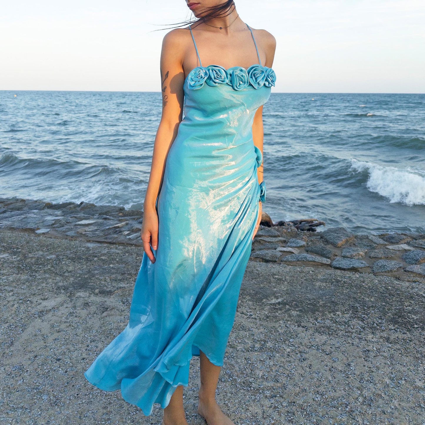 The vintage 2000s blue slip dress is a French-made fantasy with sculptural rosette appliqué along the bust and ruched side detail. Its iridescent finish and fluid midi length evoke a dreamy softness, perfect for proms, summer weddings, or romantic evenings. The silhouette is both delicate and structured, capturing quiet glamour with fairytale allure. A romantic Y2K archive crafted from a shimmering non-stretch fabric. Great vintage condition.
