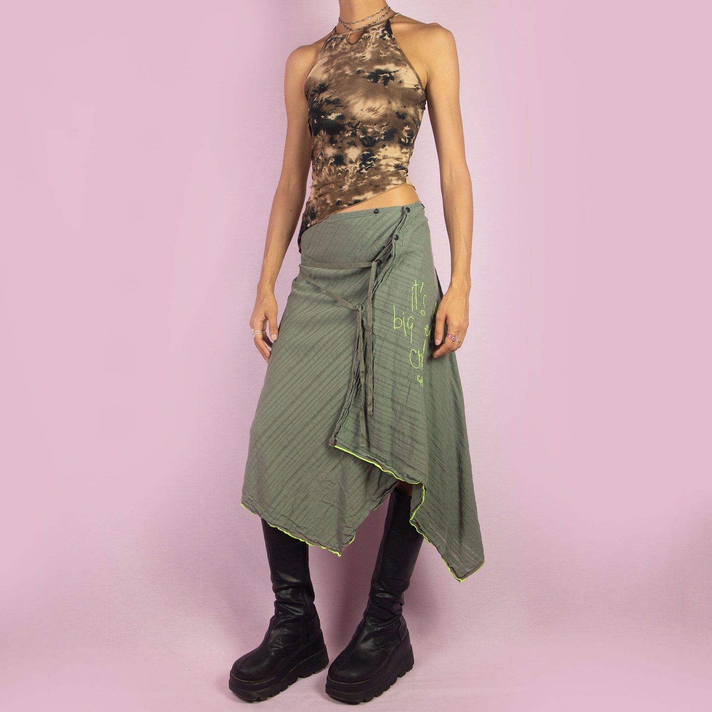 The Y2K Khaki Asymmetric Cop Copine Skirt is a unique vintage 2000s midi skirt showcasing the brand's signature avant-garde style. This high-waisted skirt features an asymmetrical hem and snap button detailing. Made with a lightweight fabric, it's an ideal choice for summer.