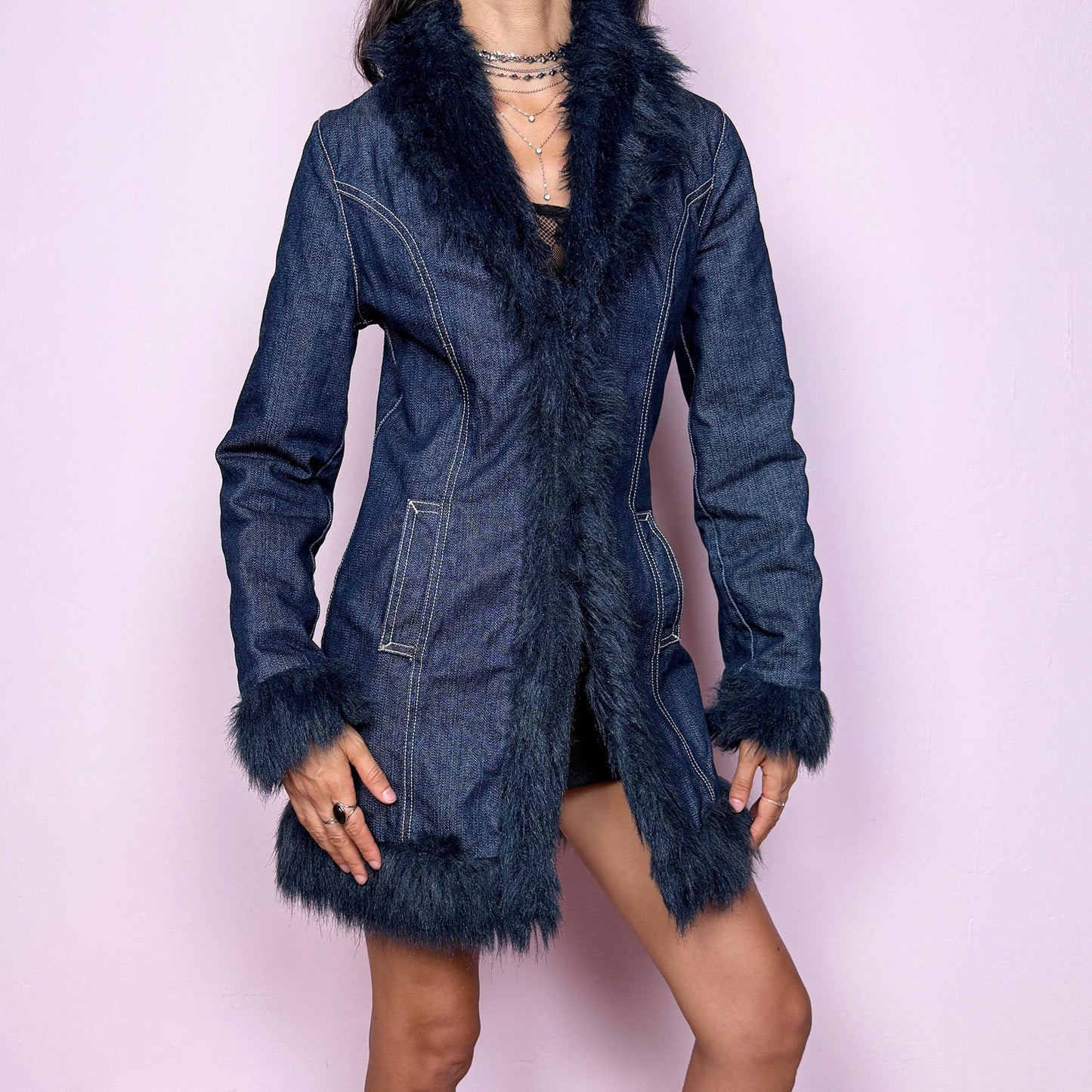 This vintage 2000s dark blue denim Penny Lane coat features deep navy faux fur trim along the collar, cuffs, and hem. Designed with front pockets and button closure, it blends 70s-inspired boho charm with Y2K streetwear edge. The fitted cut and rich indigo tone make it the ultimate statement winter coat—perfect for city styling or retro layering. Made from a cotton polyester denim blend with faux fur trim. Excellent vintage condition.