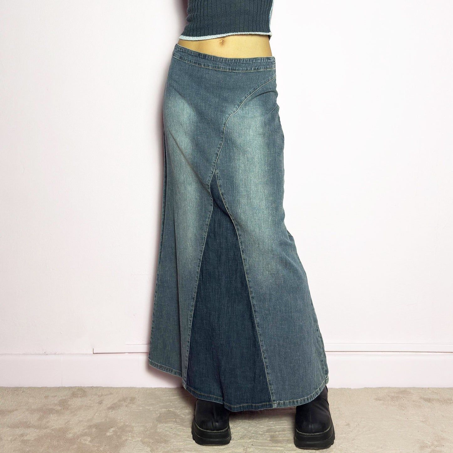 The Y2K Denim Paneled Maxi Skirt is a vintage 2000s piece featuring a unique paneled design with contrast wash details. Crafted from structured stretchy denim, this skirt offers a flattering mid-rise fit with a sleek, flared silhouette. Designed with a back zipper closure and a subtle back slit for ease of movement, it's perfect for casual streetwear outfits.