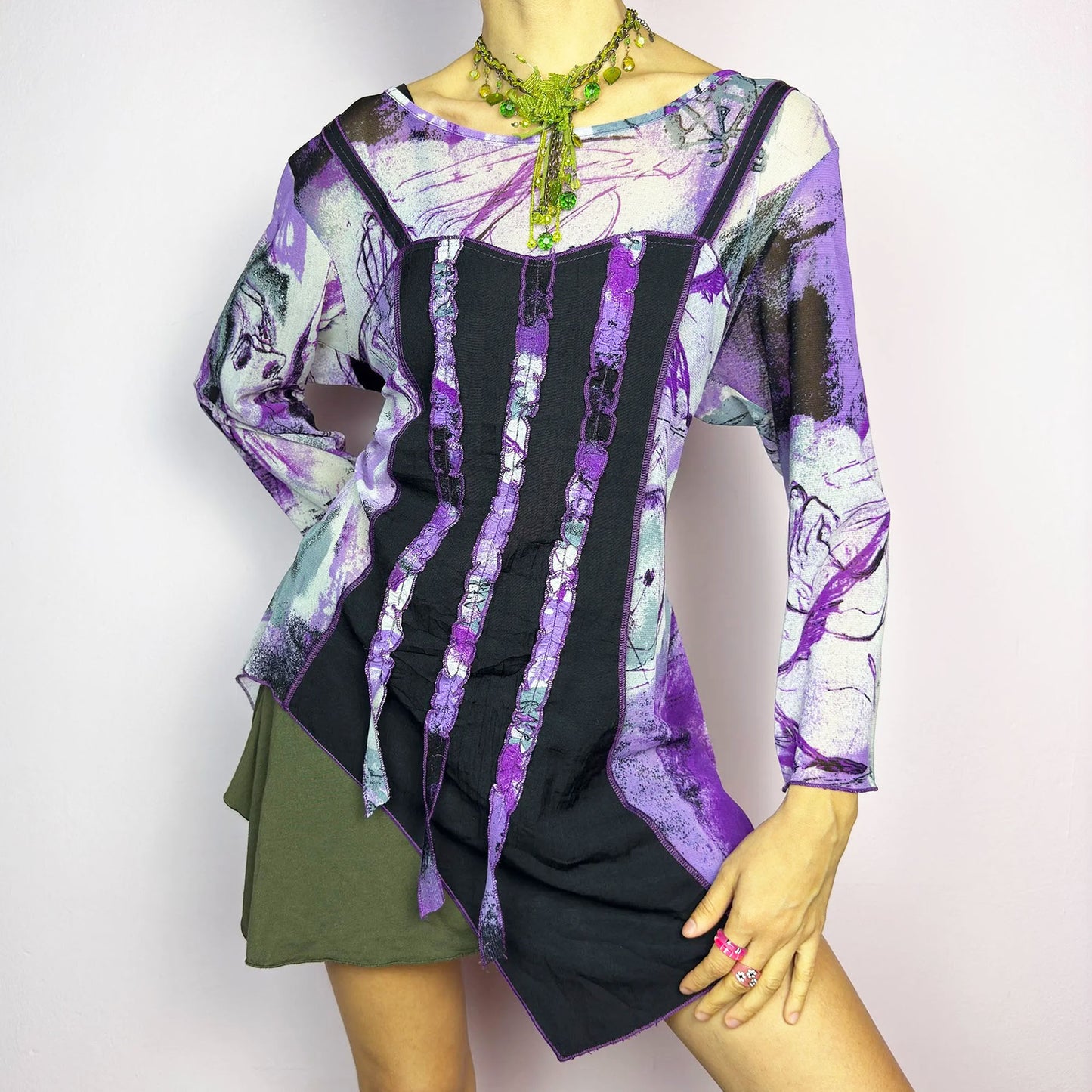 The Y2K Mesh Asymmetric Black Top is a vintage 2000s piece featuring a semi-sheer mesh fabric with an abstract purple, black, and white print. Designed with three quarter sleeves and contrast paneling and exposed seams, this top has a deconstructed, edgy aesthetic. The asymmetric hem and raw cut details add a unique touch, making it perfect for grunge or fairycore-inspired outfits. Lightweight and stretchy, ideal for layering and statement looks.