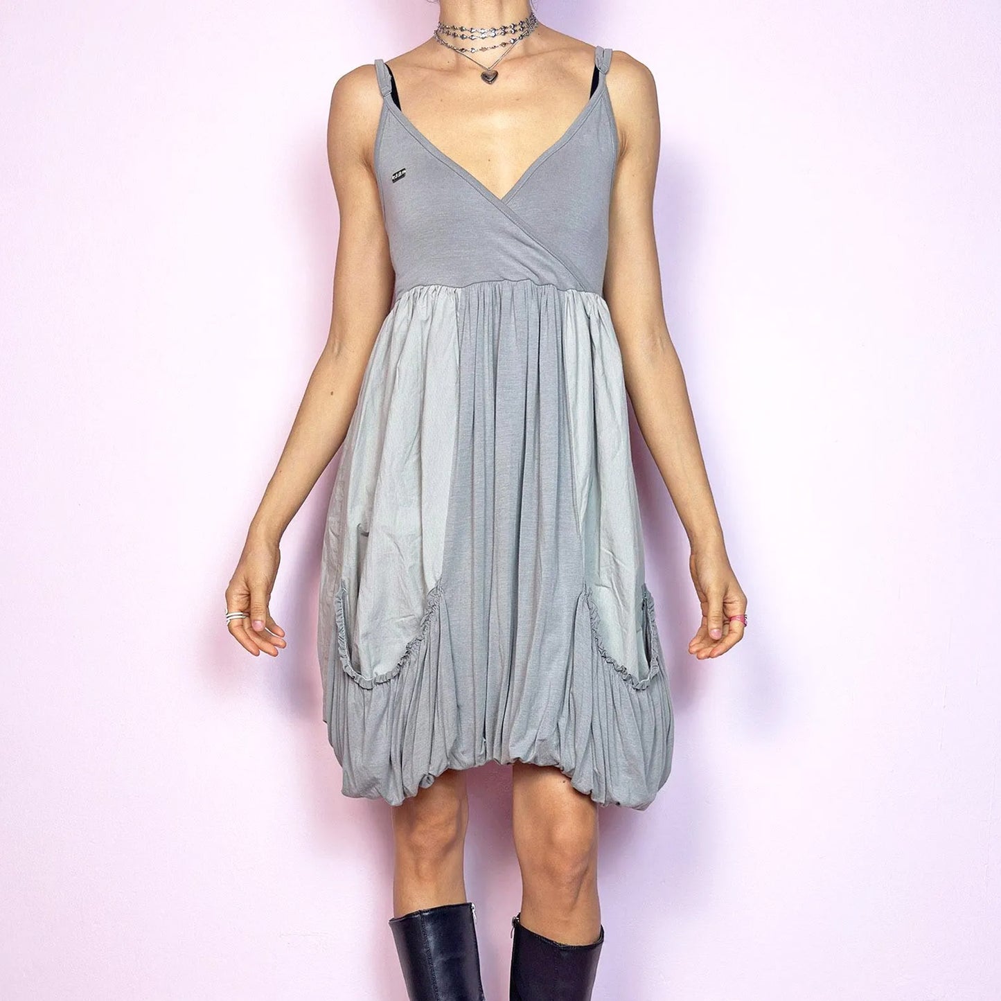 This vintage 2000s mini dress features a soft grey palette, deep wrap V-neckline, and empire waist with adjustable straps and light stretch. The voluminous bubble hem and oversized ruched pockets create sculptural movement and playful volume. Perfect for summer. A cyber-futuristic, deconstructed silhouette—airy, offbeat, and effortlessly cool. Excellent vintage condition.
