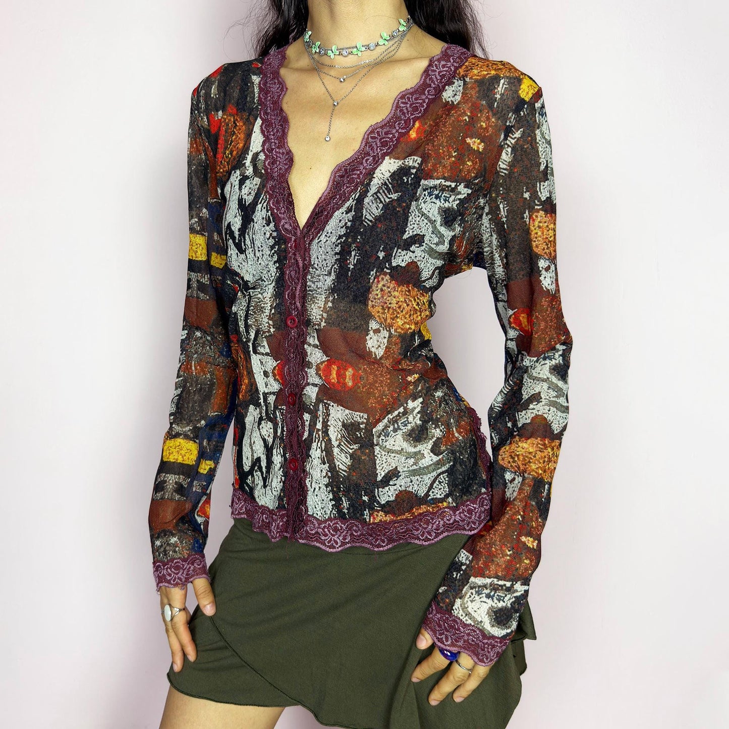 The vintage 2000s mesh sheer blouse features an abstract painting print in burnt orange, ochre, red, and charcoal. Made of stretch polyester mesh, it has long sleeves, a deep V-neckline trimmed in plum lace, and a tonal button front. This top is a rare avant garde piece with a romantic, artsy edge—perfect for chic events, layering, and transitional weather. Excellent vintage condition.