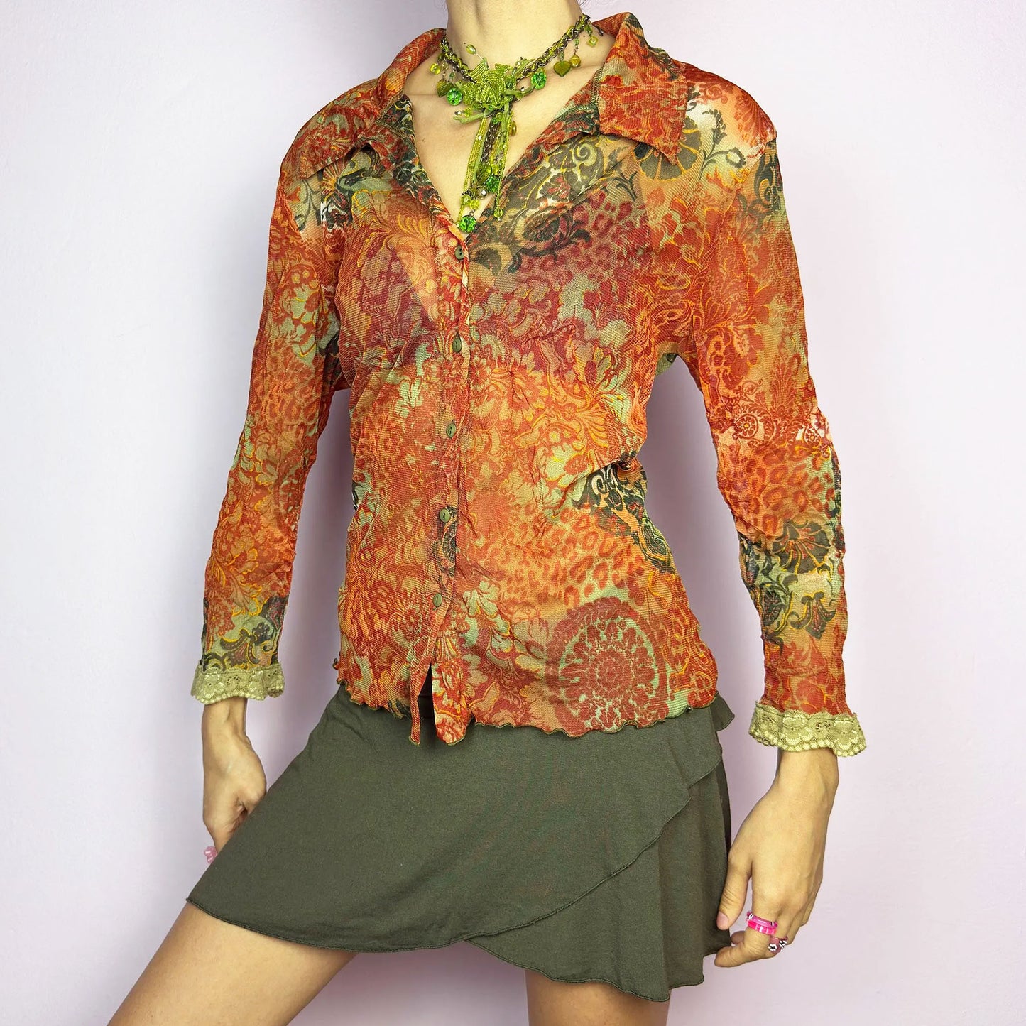 The Y2K Baroque Print Mesh Blouse is a vintage 2000s piece featuring a semi-sheer mesh fabric with a rich baroque-inspired floral print in warm tones. Designed with a fitted silhouette, button-up front, delicate lace trim on the cuffs and three quarter sleeves, the lightweight and stretchy fabric make it ideal for summer bohemian-inspired looks.