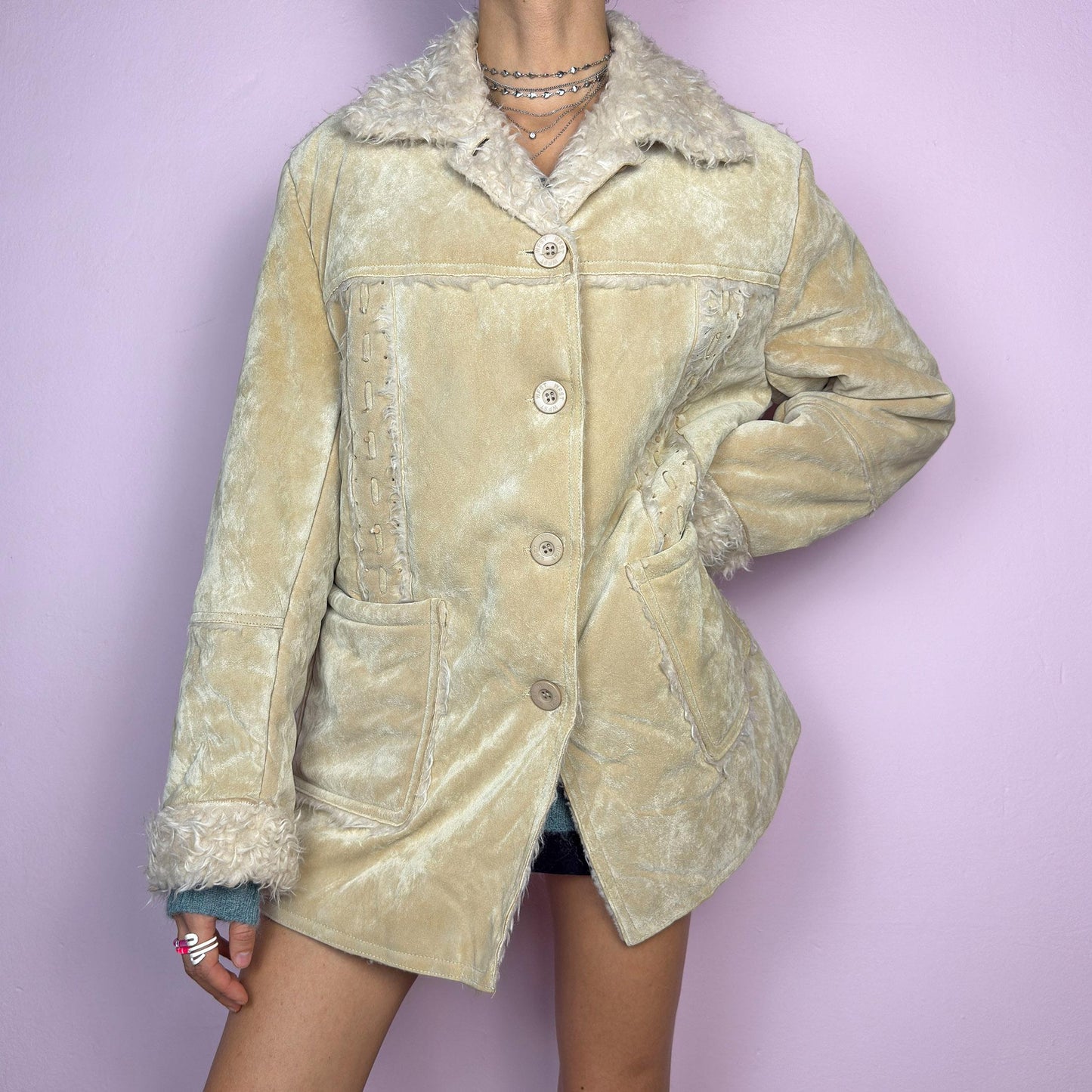The Y2K Beige Faux Fur Suede Jacket is a vintage 2000s cozy outerwear piece featuring a soft faux suede finish in a beige tone, a faux shearling-lined collar and cuffs for added warmth, a button-front closure and pockets. adult world shop