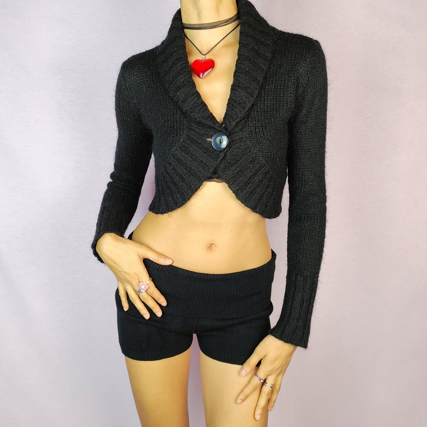 The Y2K Black Cropped Bolero Cardigan is a vintage 2000s piece featuring a chic single-button front closure and a shawl collar. This bolero-style cardigan is crafted from a soft knit fabric and the cropped silhouette makes it perfect for layering.