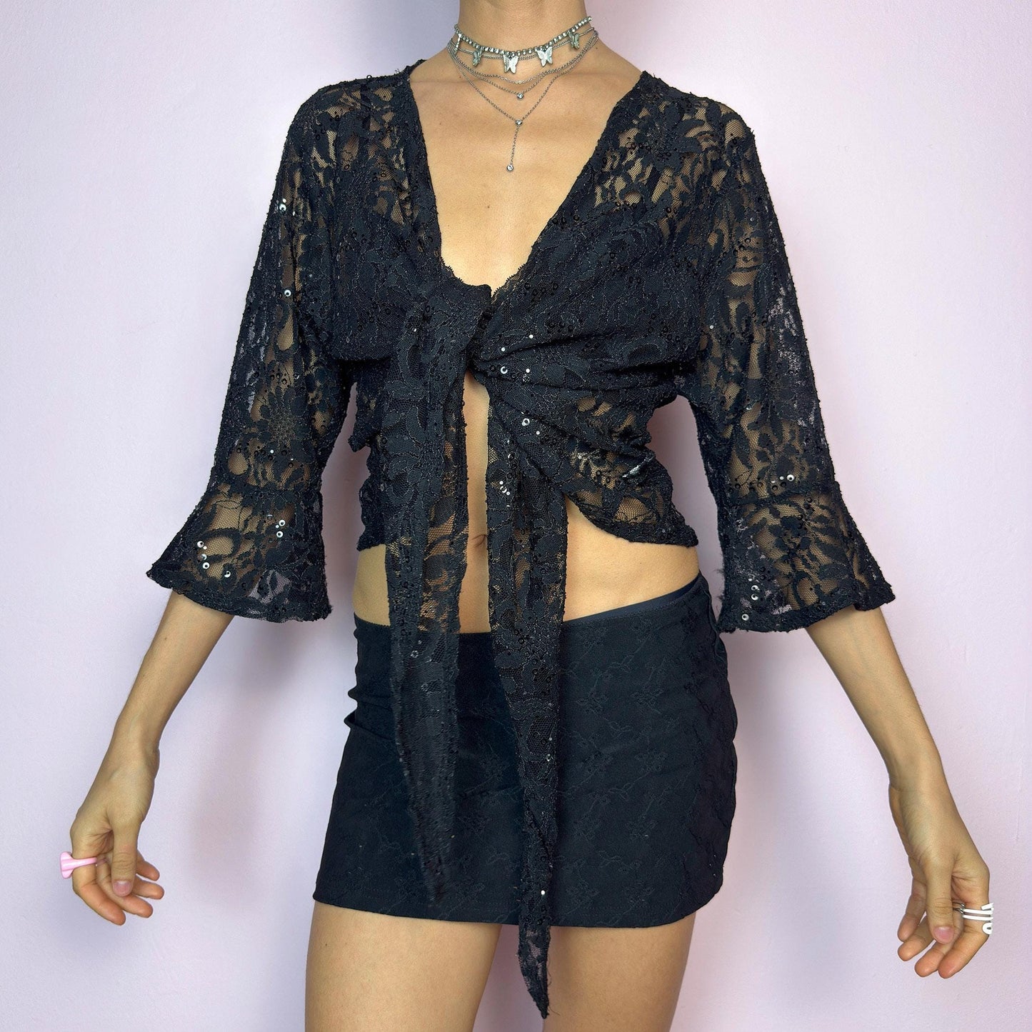 The Y2K Black Lace Tie Bolero is a vintage 2000s sheer tie-front top crafted in delicate floral lace with subtle sequin accents. Features flared three-quarter sleeves for a dreamy silhouette and an adjustable tie at the front for versatile styling. Ideal for summer nights, festivals, or clubwear looks. adult world shop