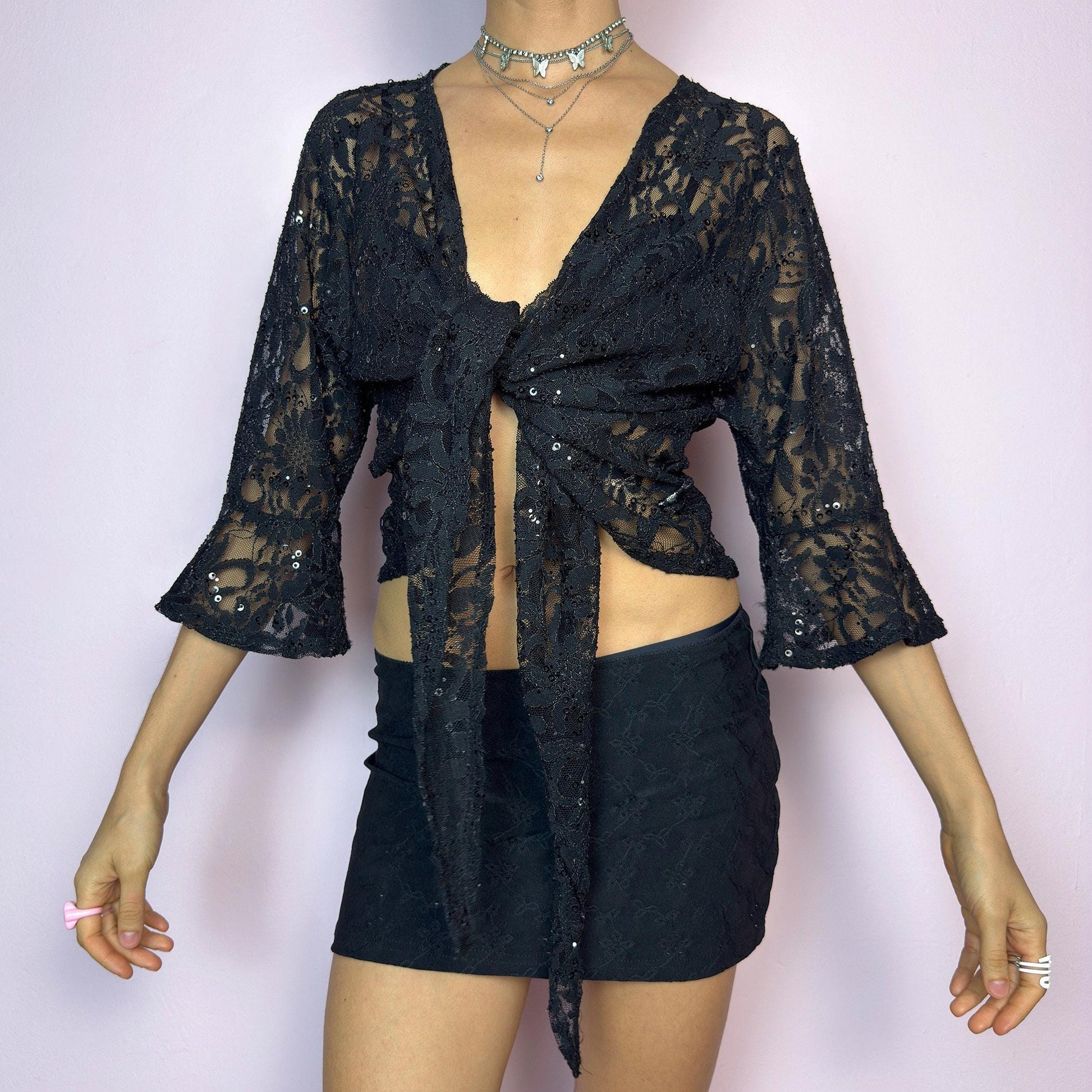 The Y2K Black Lace Tie Bolero is a vintage 2000s sheer tie-front top crafted in delicate floral lace with subtle sequin accents. Features flared three-quarter sleeves for a dreamy silhouette and an adjustable tie at the front for versatile styling. Ideal for summer nights, festivals, or clubwear looks. adult world shop
