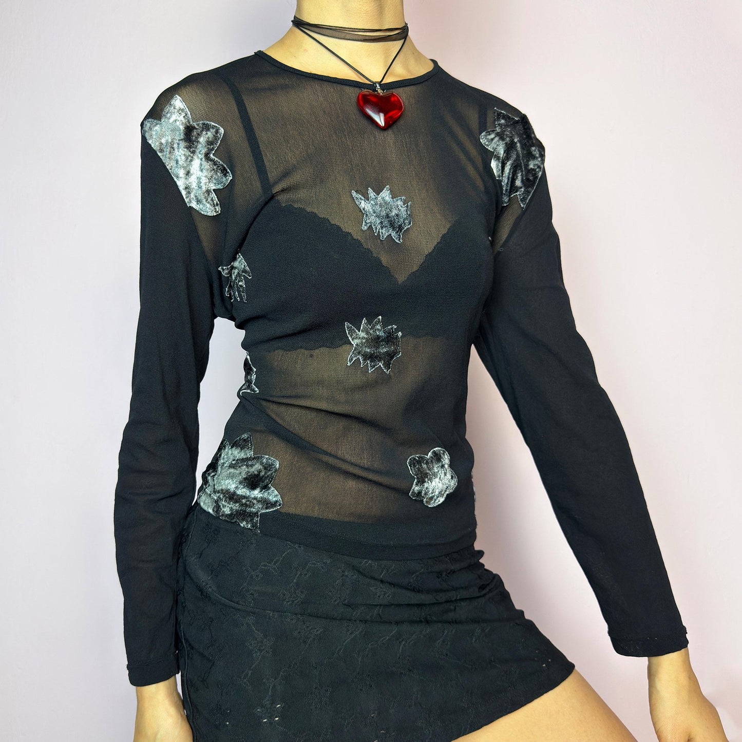 The Y2K Black Mesh Appliqué Top is a vintage 2000s sheer black mesh top featuring abstract velvet appliqués in silver tones across the front, a fitted silhouette with long sleeves and soft stretch fabric. Eye-catching and edgy – ideal for layering, night out looks, or styled as rave, grunge, or clubwear. Great vintage condition. adult world shop