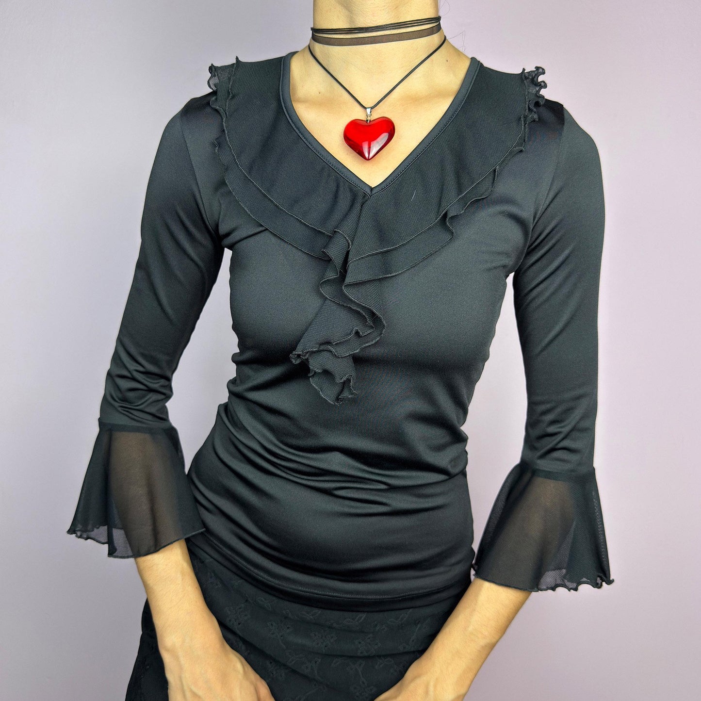 The Y2K Black Ruffle Bell Sleeve Top is a sleek and elegant vintage 2000s piece. Featuring a fitted silhouette with cascading ruffles along the neckline and a flattering V-neck design. The three-quarter bell sleeves with sheer mesh. adult world shop