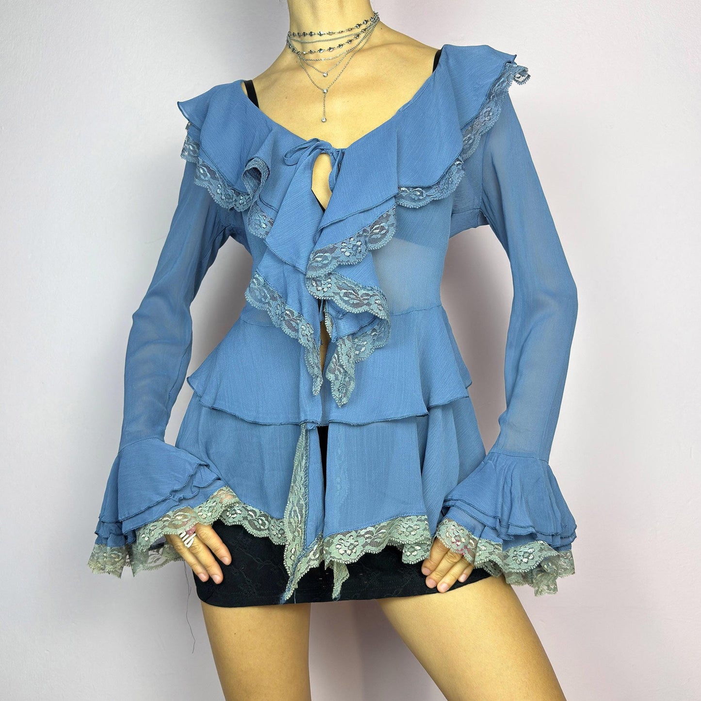 The Y2K Blue Ruffle Blouse is a dreamy vintage 2000s piece with a romantic and ethereal aesthetic. Crafted from a sheer, lightweight fabric in a soft blue shade, this blouse features cascading ruffles with delicate lace trim. adult world shop